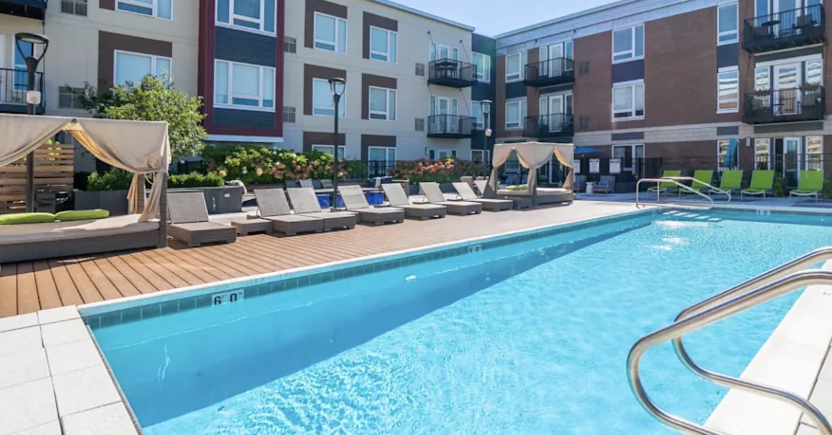Resort-style swimming pool with lounge chairs, cabanas, and multi-story apartment buildings surrounding a courtyard.
