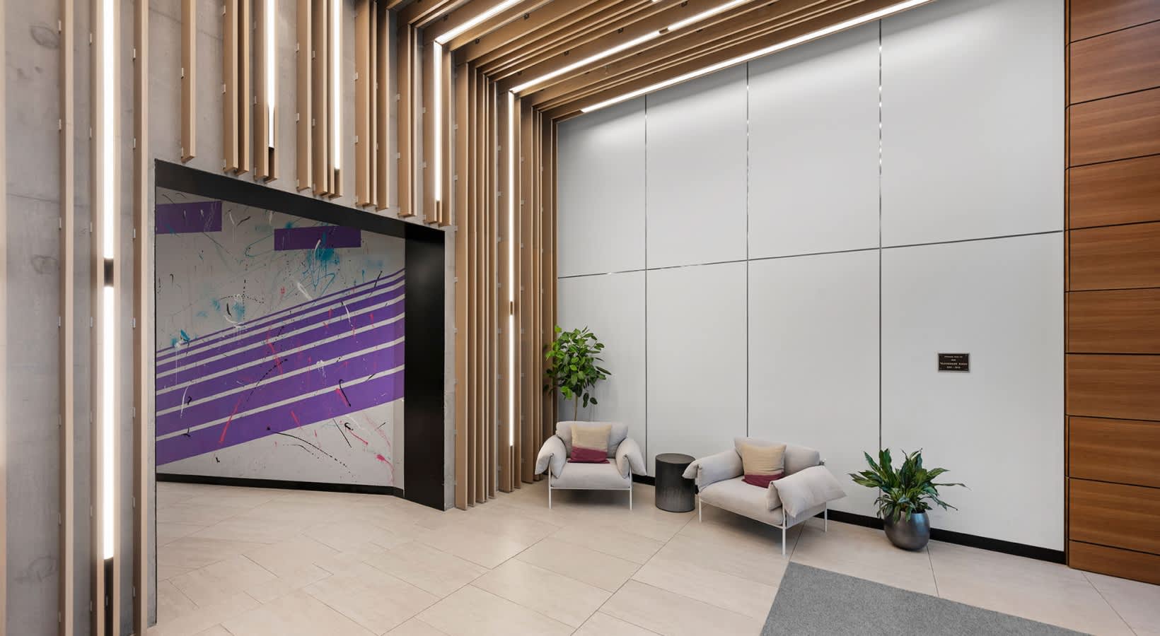 Modern lounge with cream and gray seating, potted plants, large wall-mounted screen with purple graphic, and linear ceiling lights.