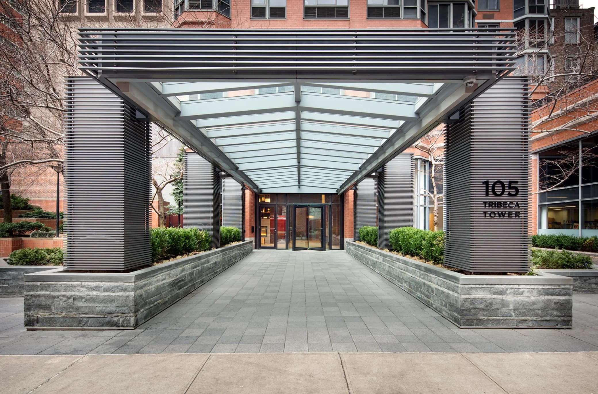 Glass and metal canopy entrance with stone planters, leading to building doors at Tribeca Tower.