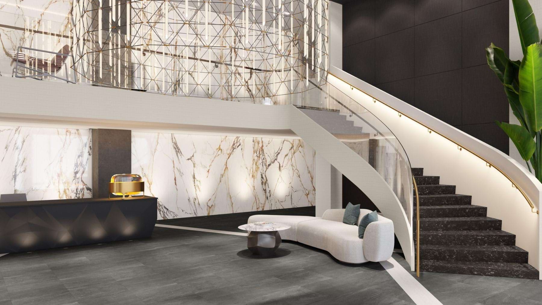 Modern lobby with white curved sofa, marble wall paneling, dark staircase with handrail, and geometric pendant light fixture.