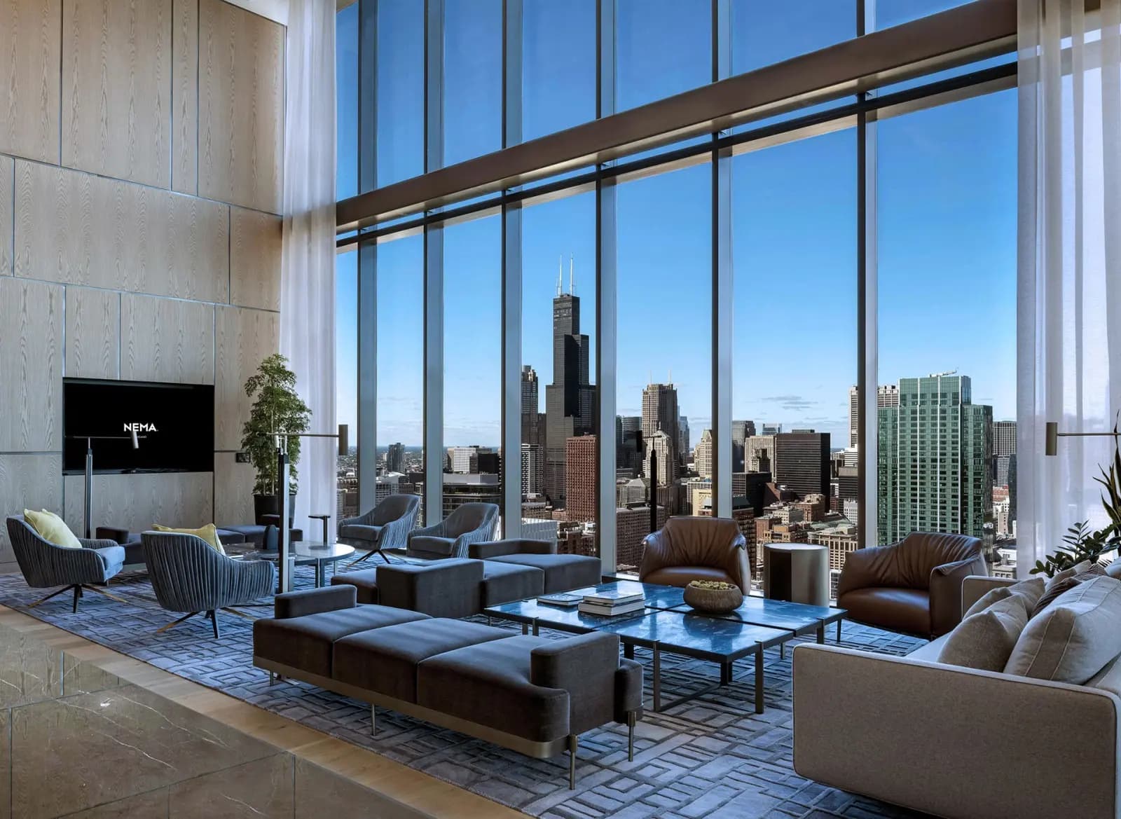Modern lounge with floor-to-ceiling windows overlooking Chicago skyline, featuring contemporary seating, blue area rug, and potted plants.