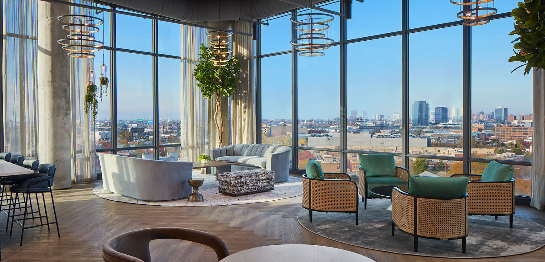 High-rise lounge with floor-to-ceiling windows overlooking Chicago skyline, curved seating areas, hanging plants, and mid-century modern furniture.