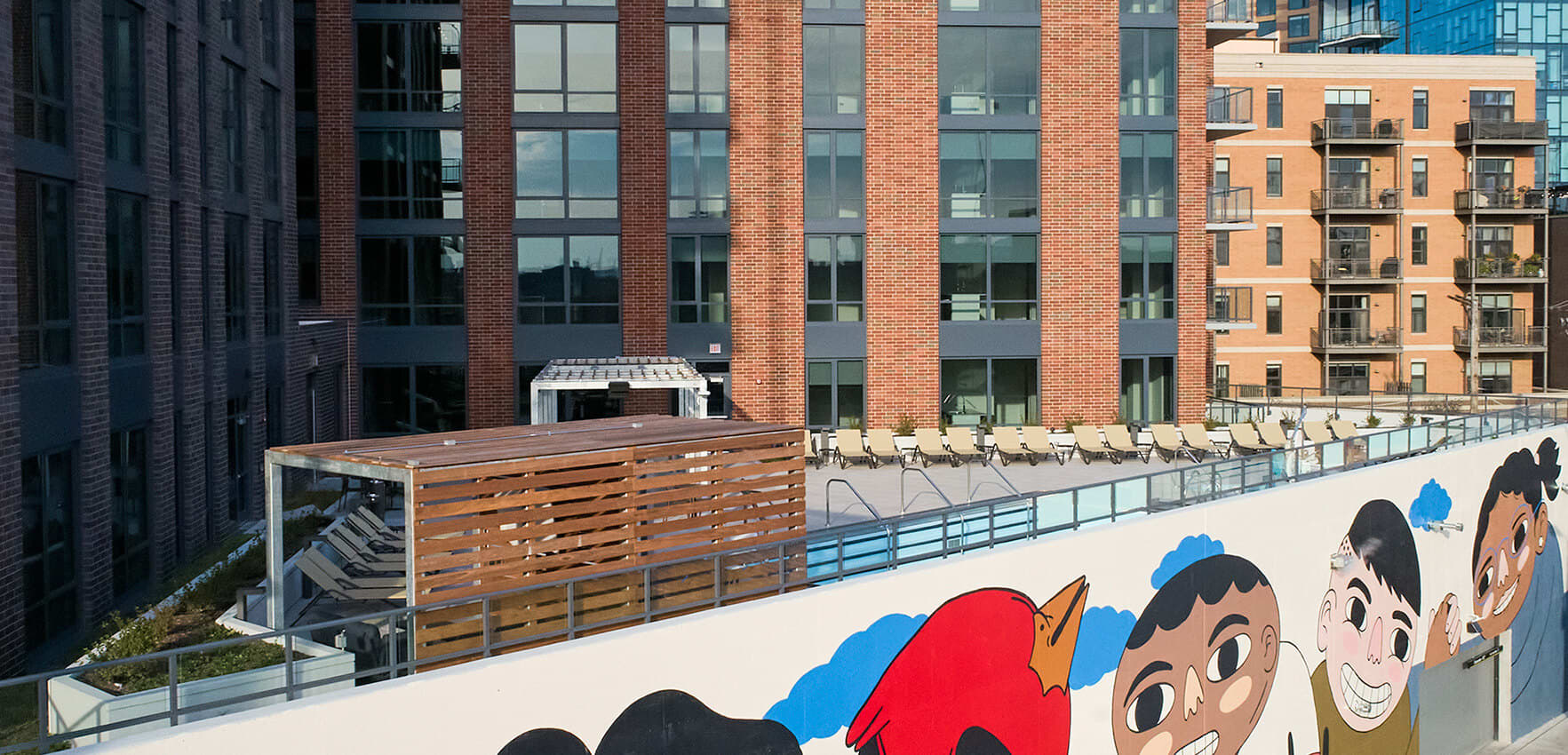 Rooftop terrace with wooden privacy screens, lounge chairs, metal railings, and colorful mural overlooking brick buildings.