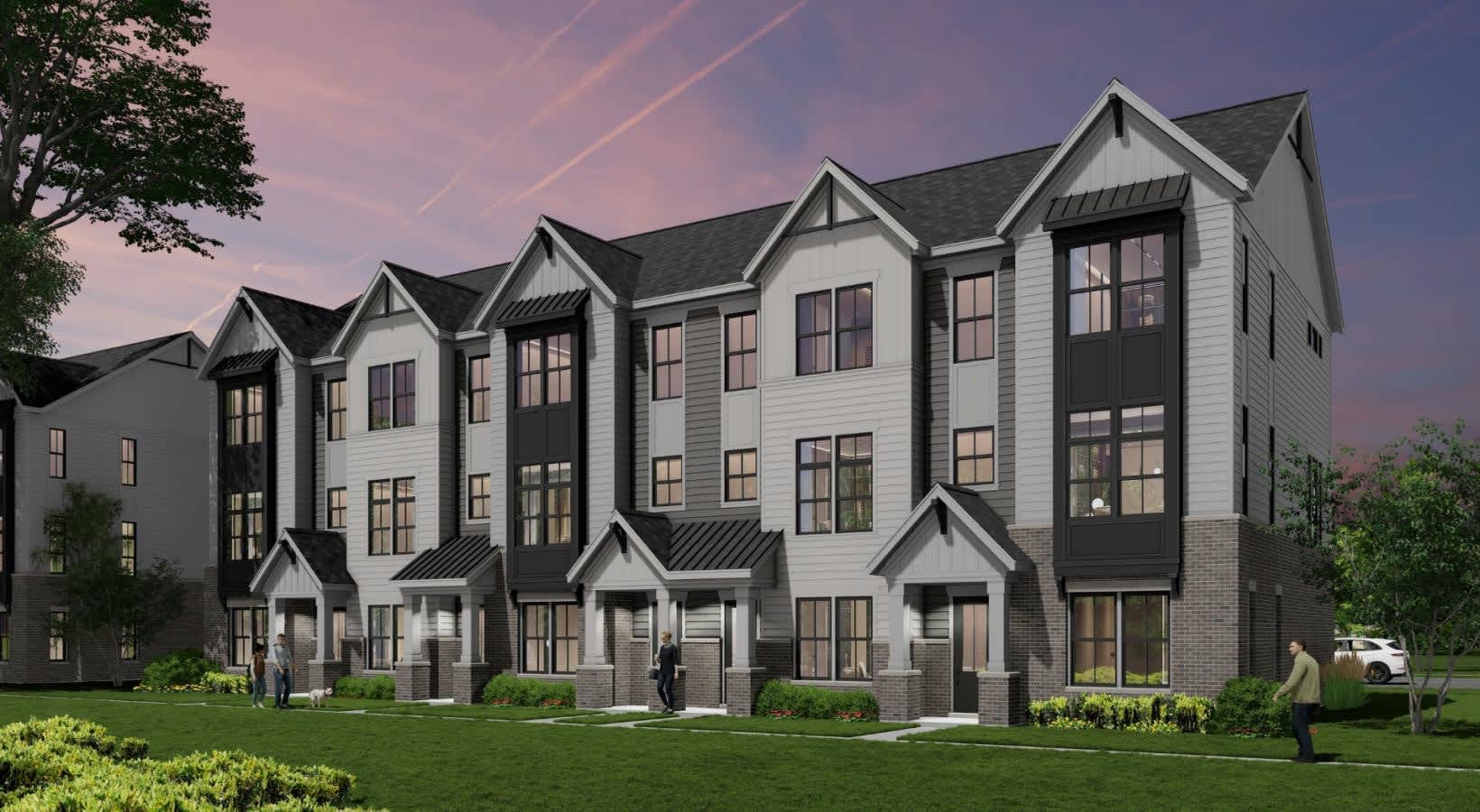 Row of contemporary townhomes with white siding, dark brick accents, peaked gables, and tall windows at dusk.