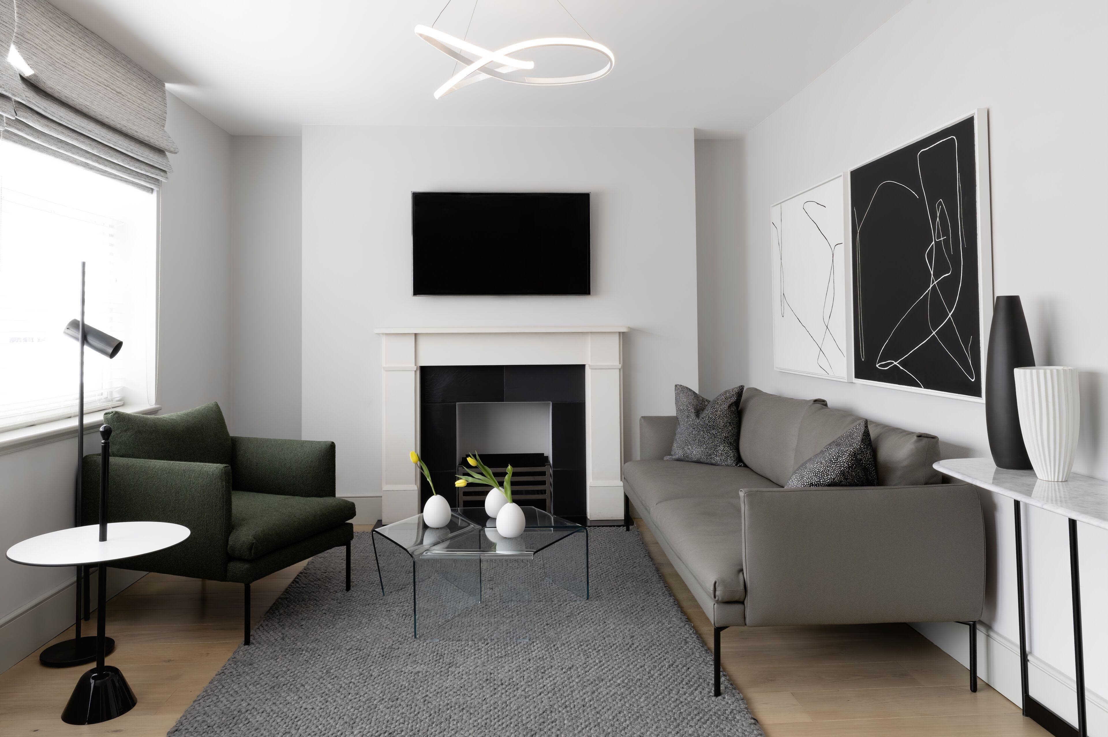 Contemporary living room with gray sofa, green armchair, fireplace with black insert, wall-mounted TV, and abstract artwork.