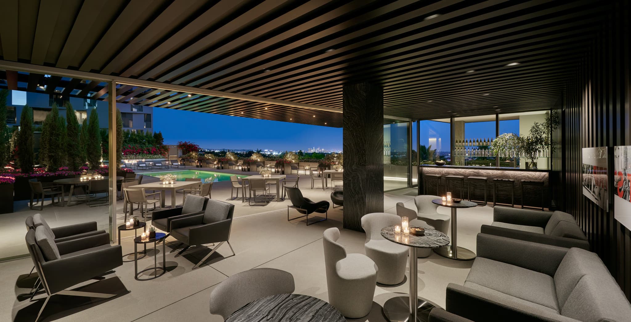 Rooftop lounge at dusk with contemporary seating, round tables, pool area, and West Hollywood skyline views.