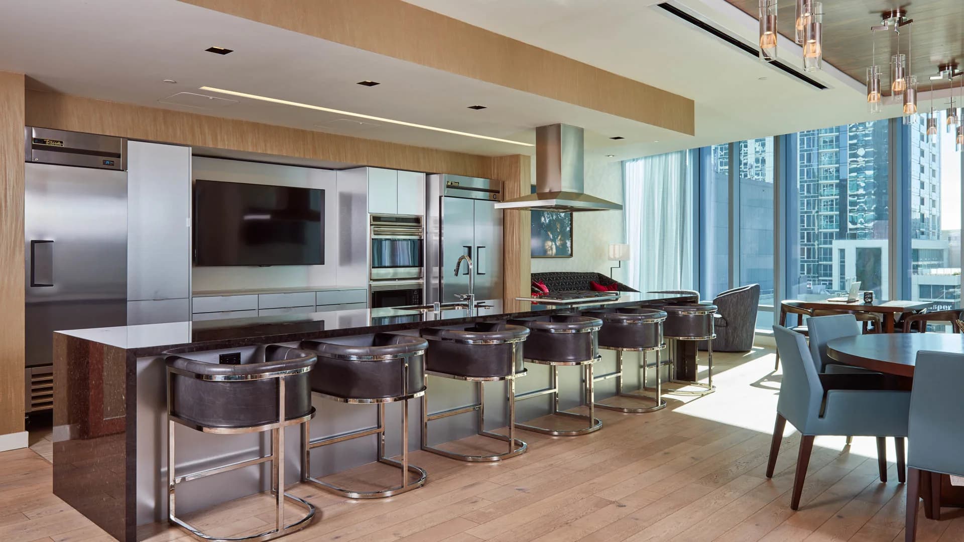 Modern kitchen with dark wood island, stainless steel appliances, bar seating for five, and expansive city views through floor-to-ceiling windows.