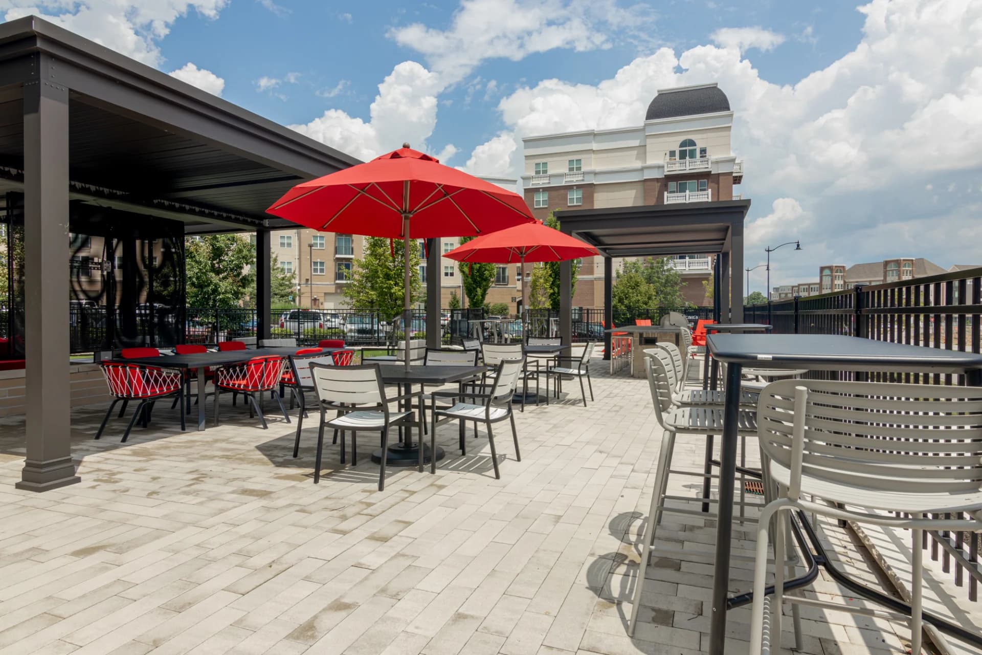 Rooftop terrace with red umbrellas, black pergolas, dining tables, and chairs overlooking Carmel buildings and streets.