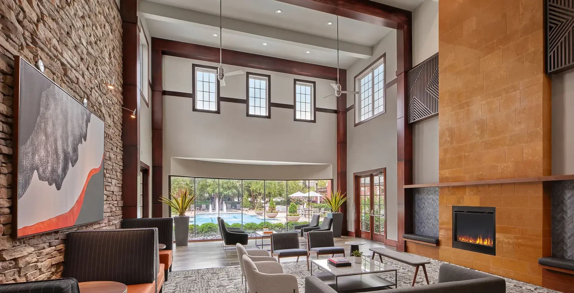 Two-story living room with high ceilings, exposed brick wall, orange accent wall, fireplace, and floor-to-ceiling windows overlooking courtyard.