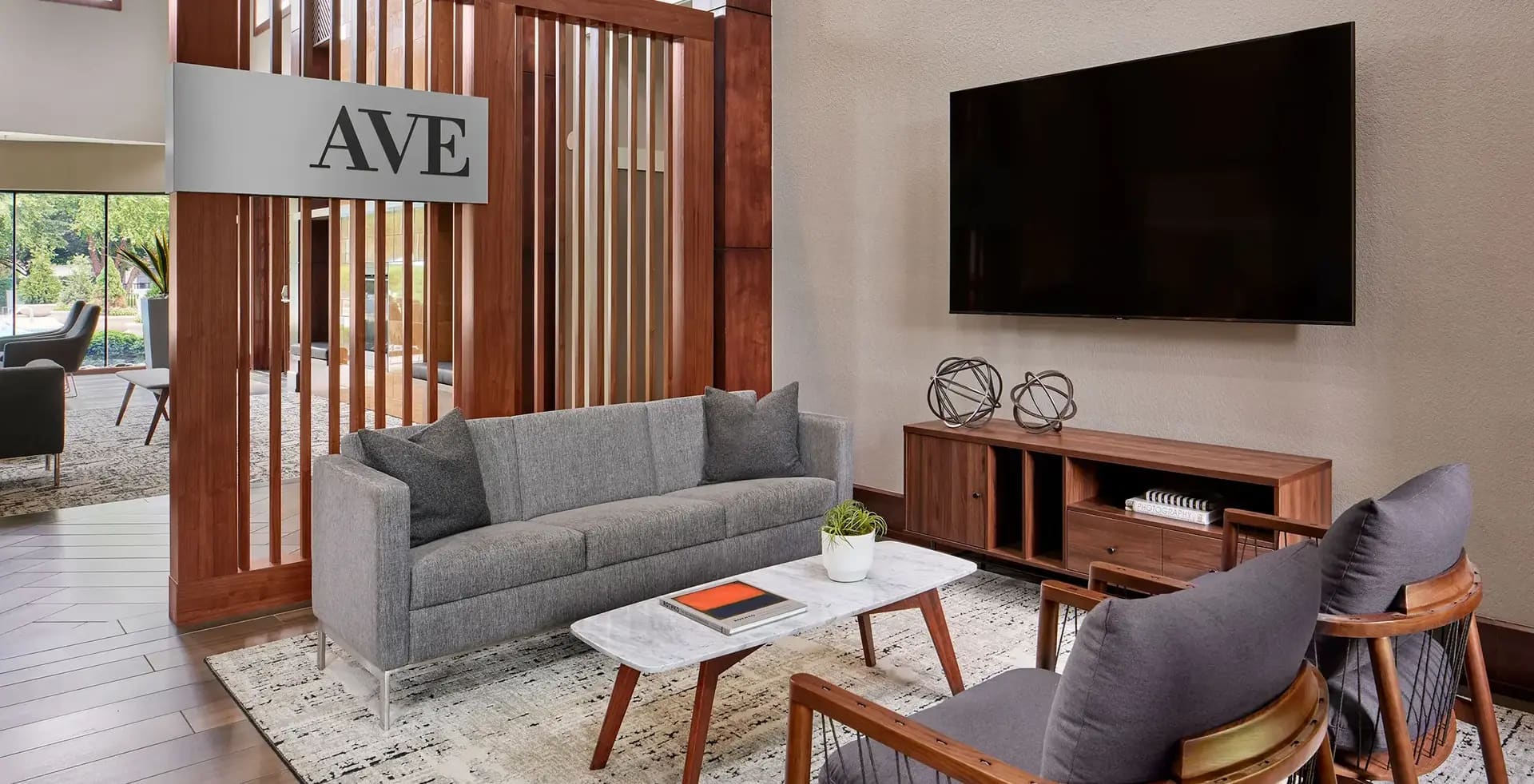 Modern living room with gray upholstered sofa, white marble coffee table, wood media console with TV, and wooden room divider.
