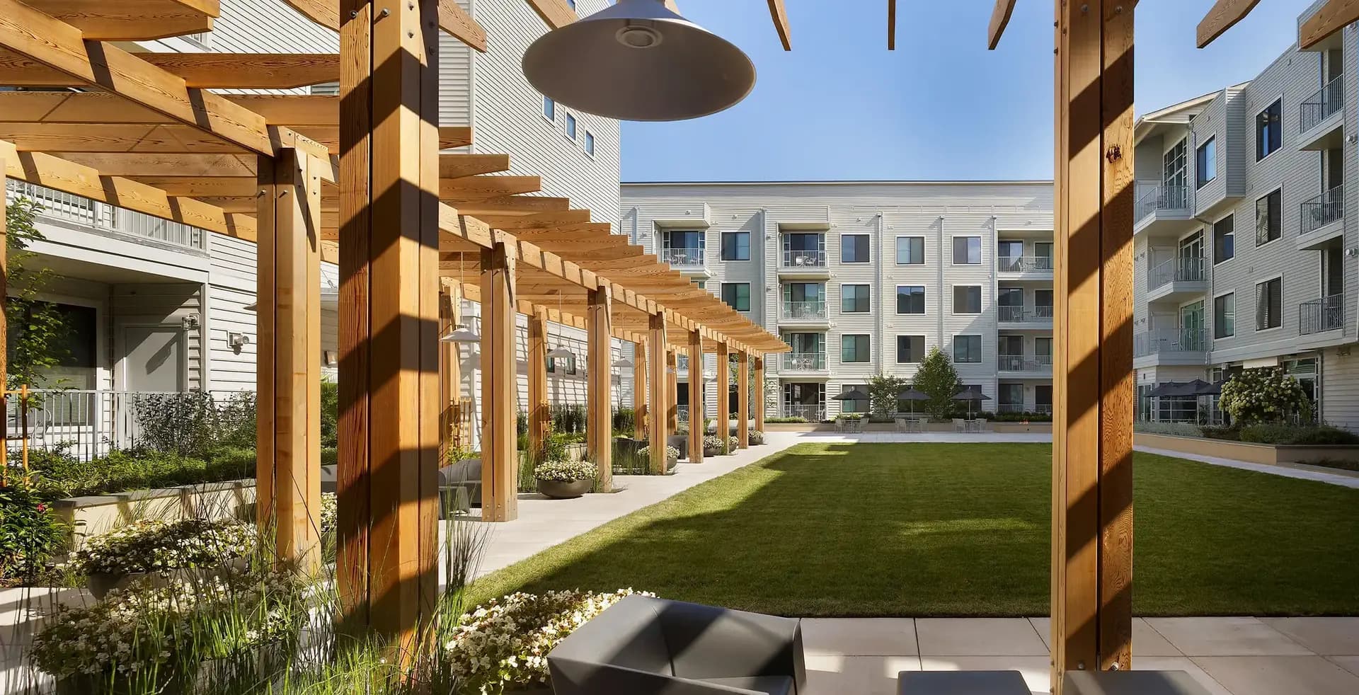 Wooden pergola with hanging pendant light overlooking green courtyard lawn and surrounding apartment buildings in Union, NJ.