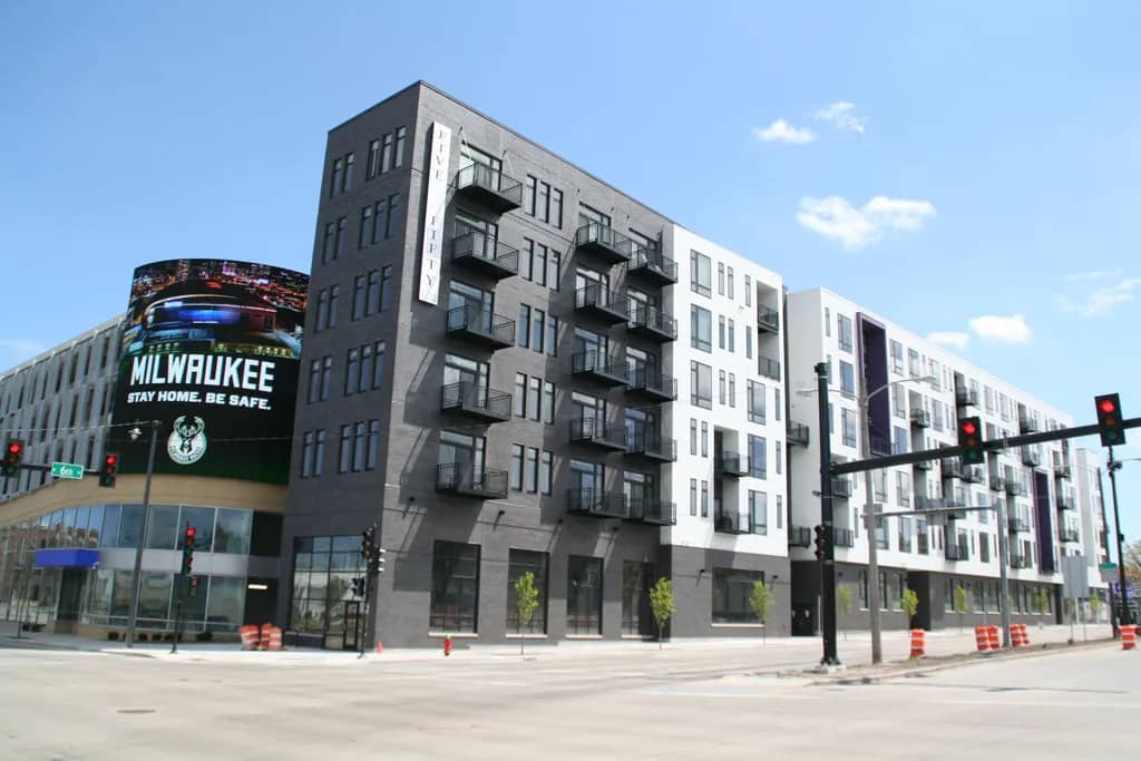 Modern mixed-use building with white and dark gray facade, multiple balconies, and ground-floor retail in downtown Milwaukee.