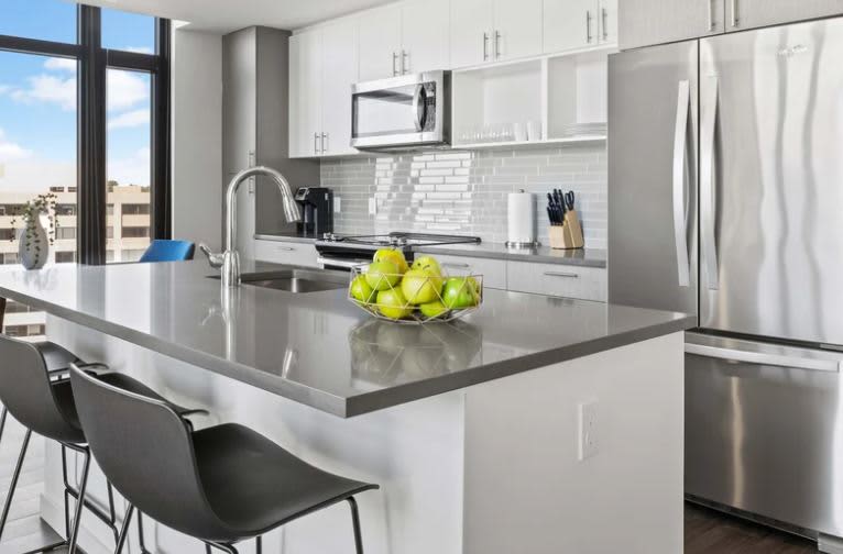 Modern kitchen with white cabinets, gray quartz island countertop, stainless steel appliances, subway tile backsplash, and floor-to-ceiling windows overlooking the city.