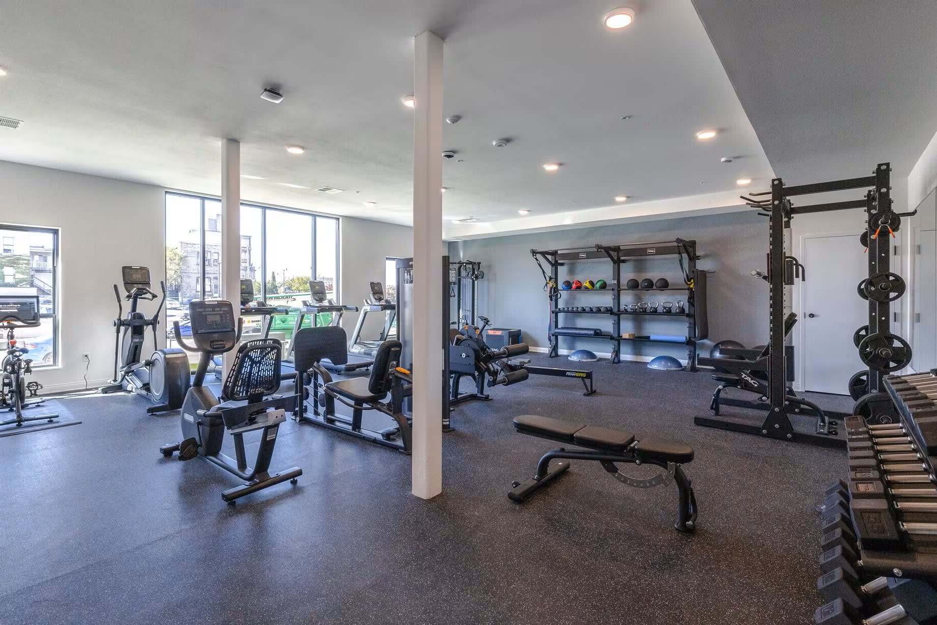 Spacious fitness center with exercise bikes, weight racks, dumbbells, and strength training machines under recessed lighting.