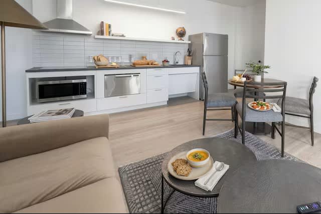 Modern kitchen with white cabinetry, stainless steel appliances, and dining table with two chairs in open-plan living space.