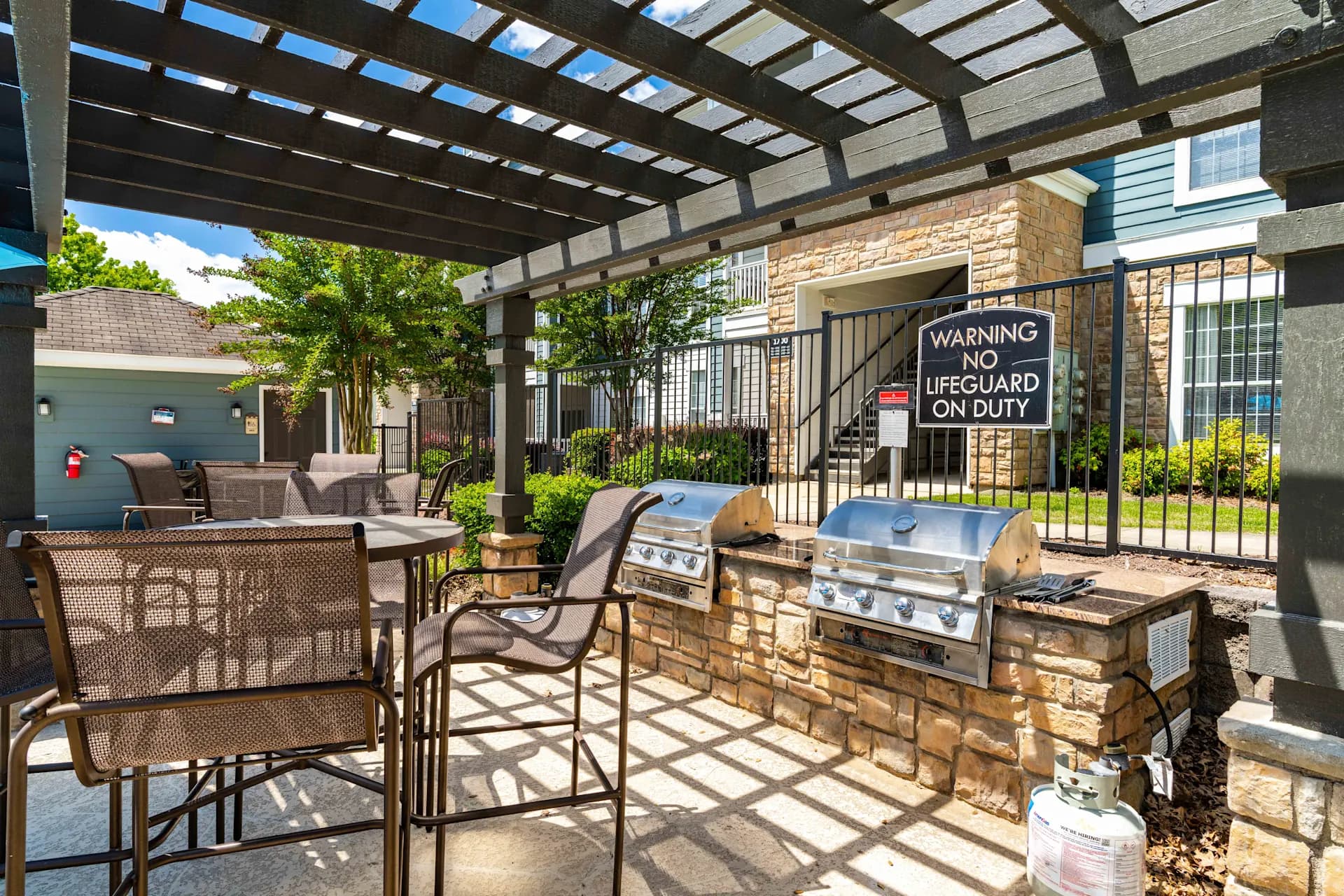 Covered patio with two stainless steel grills built into a brick counter, lounge chairs, and pergola overhead.