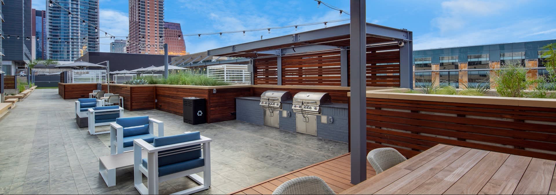 Rooftop patio with white and blue built-in benches, stainless steel grills, wood pergola, and downtown Austin skyline.