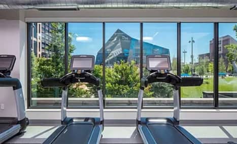 Fitness room with two treadmills facing large windows with views of downtown Minneapolis buildings and trees.