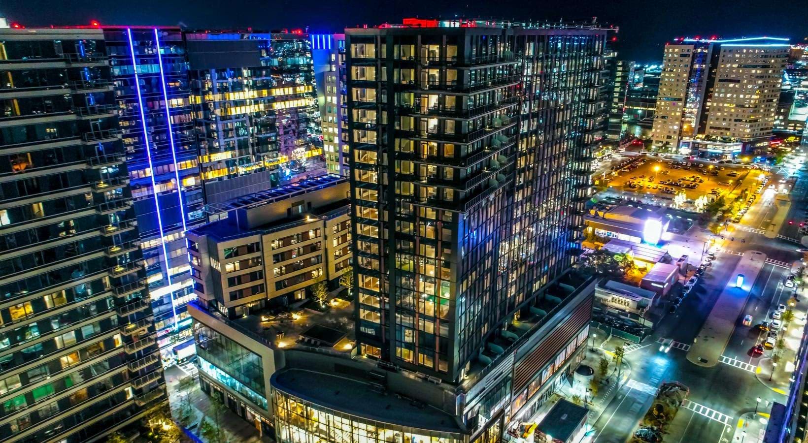 Nighttime aerial view of downtown Boston with illuminated high-rise residential and office buildings surrounding a central courtyard and street-level retail.