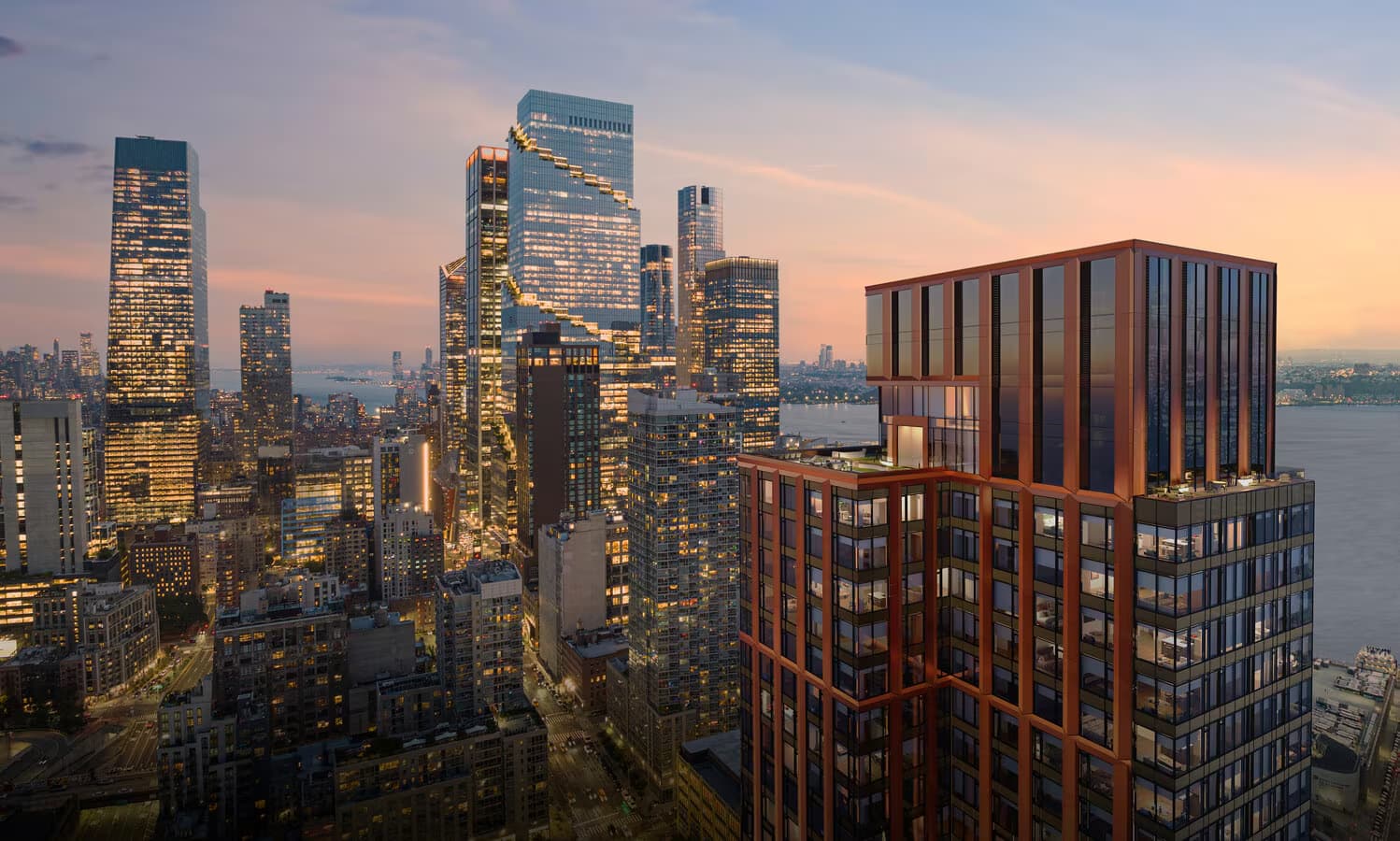 Modern residential building with red brick and glass facade overlooking illuminated Manhattan skyscrapers and Hudson River at dusk.