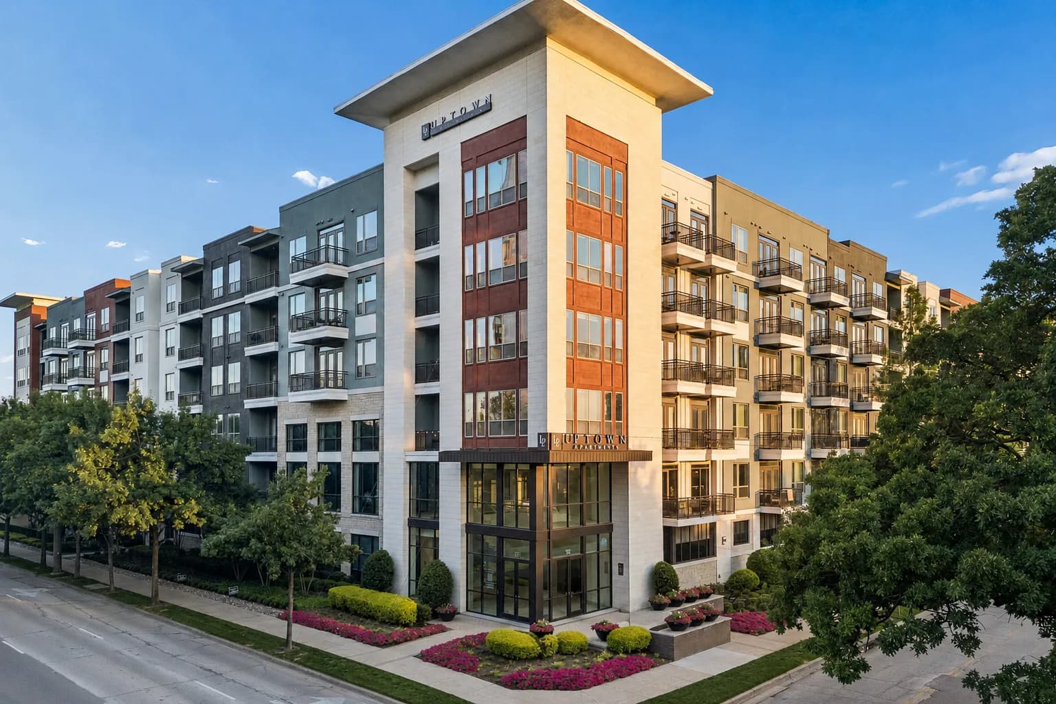 Contemporary multi-story apartment building with cream, gray, and rust-colored facades, ground-floor retail space, and manicured landscaping with flowering shrubs.