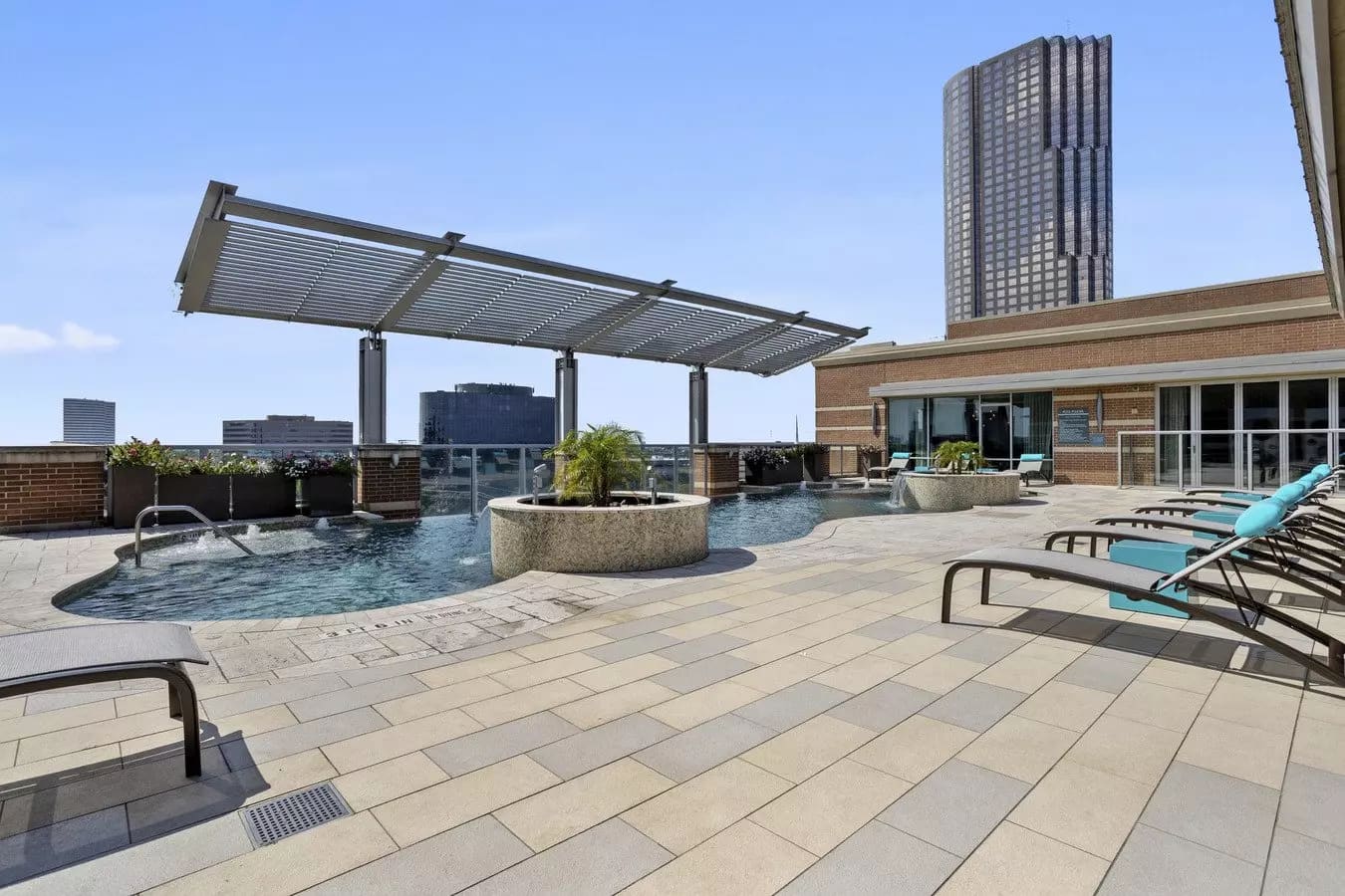 Rooftop pool area with lounge chairs, pergola, and downtown Houston skyline in background.