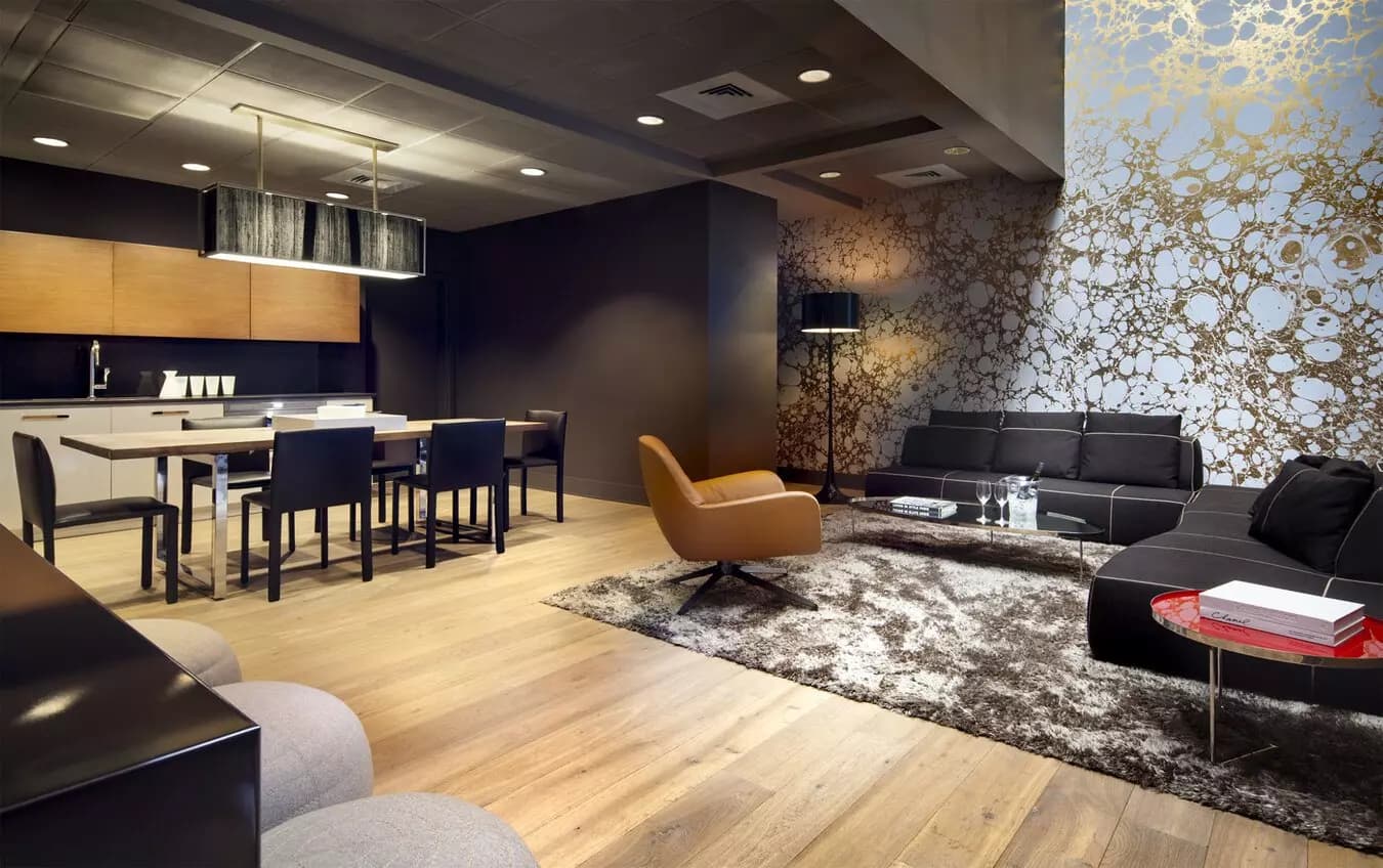 Open-concept apartment with wood flooring, navy kitchen with island, black sectional sofa, tan accent chair, and patterned accent wall.