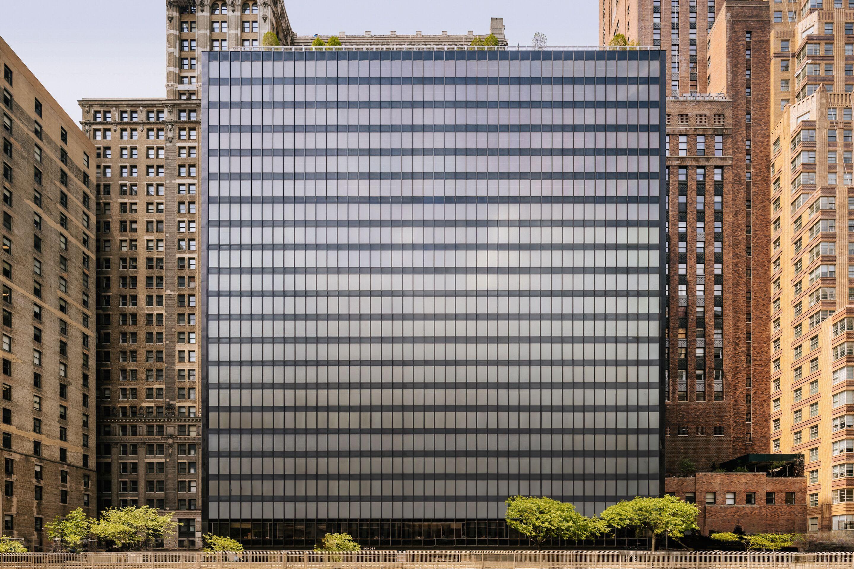 Modern glass and steel office building surrounded by historic brick buildings and green landscaping in downtown Manhattan.