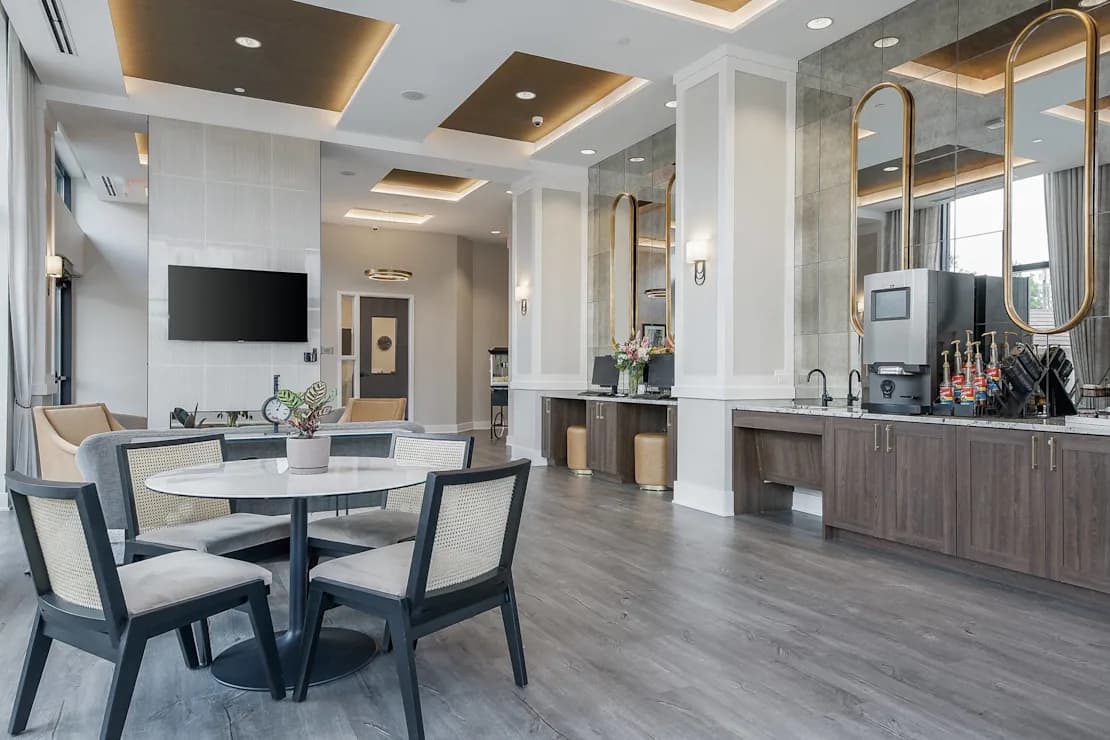 Open-concept living space with round dining table, dark wood kitchen cabinetry, gold-framed mirror, and coffered ceiling with recessed lighting.