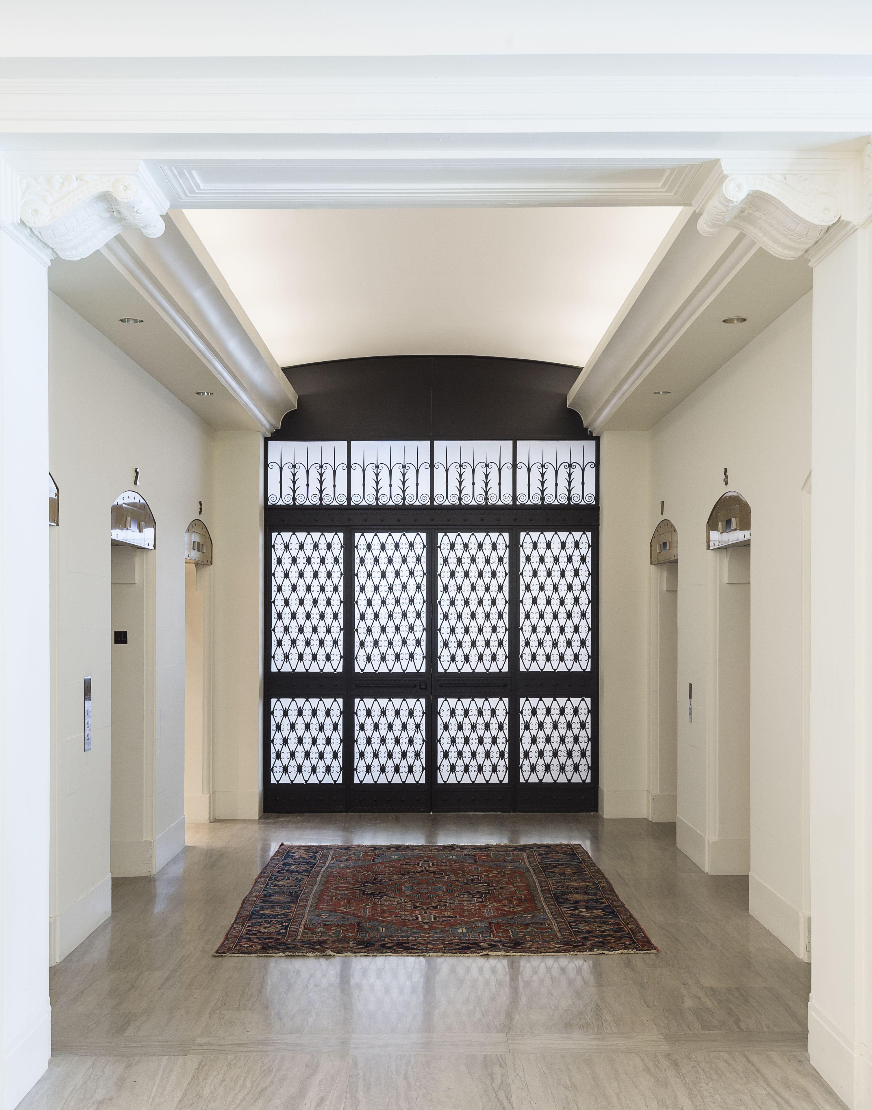 Foyer with cream walls, black patterned double doors, brass wall sconces, and light wood flooring with an area rug.