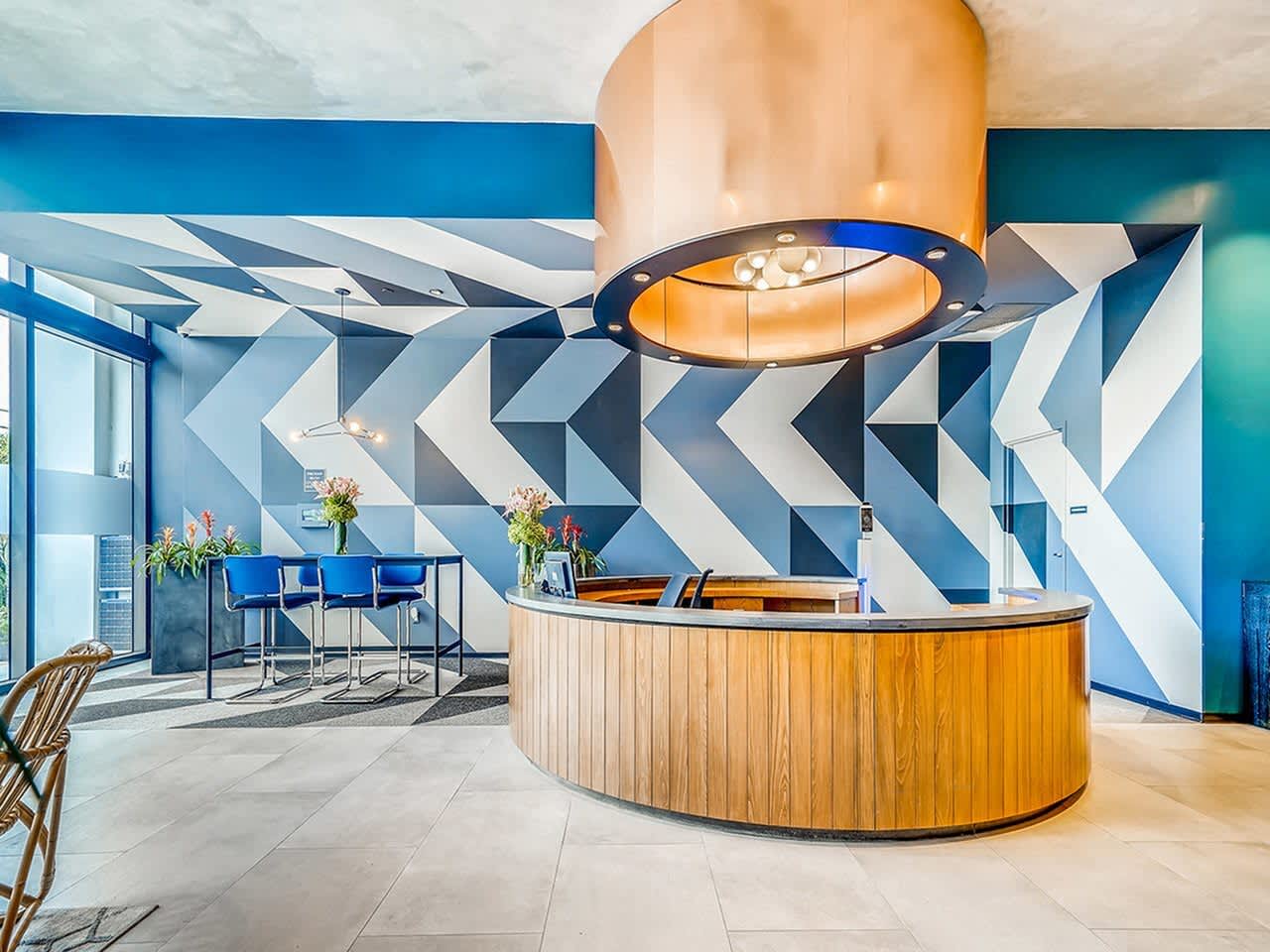 Modern lobby with curved wooden reception desk, geometric blue and white wall pattern, and sculptural pendant light fixture.