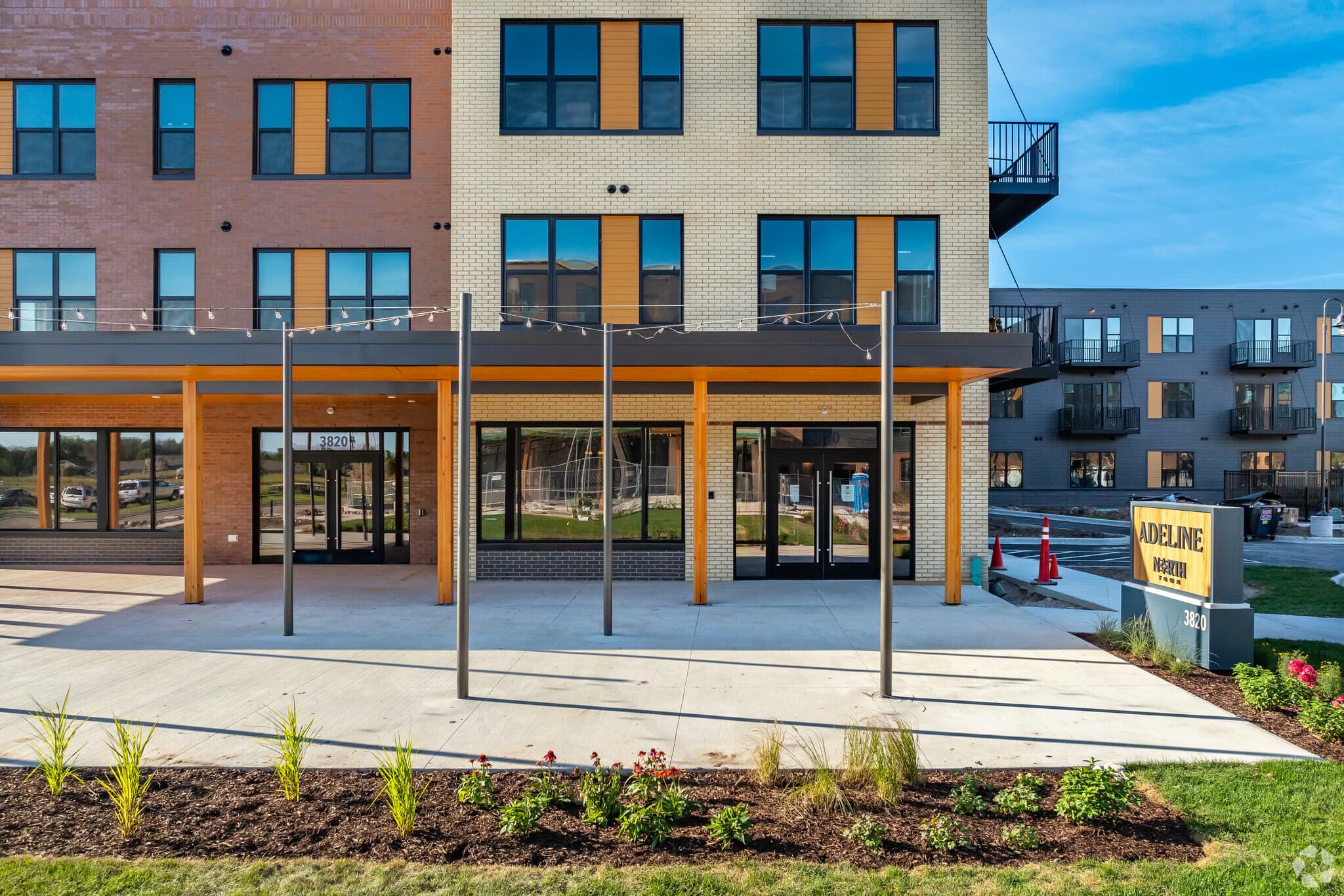 Ground-floor commercial space with wood pergola, glass storefronts, and multi-story brick apartment building with blue-trimmed windows.