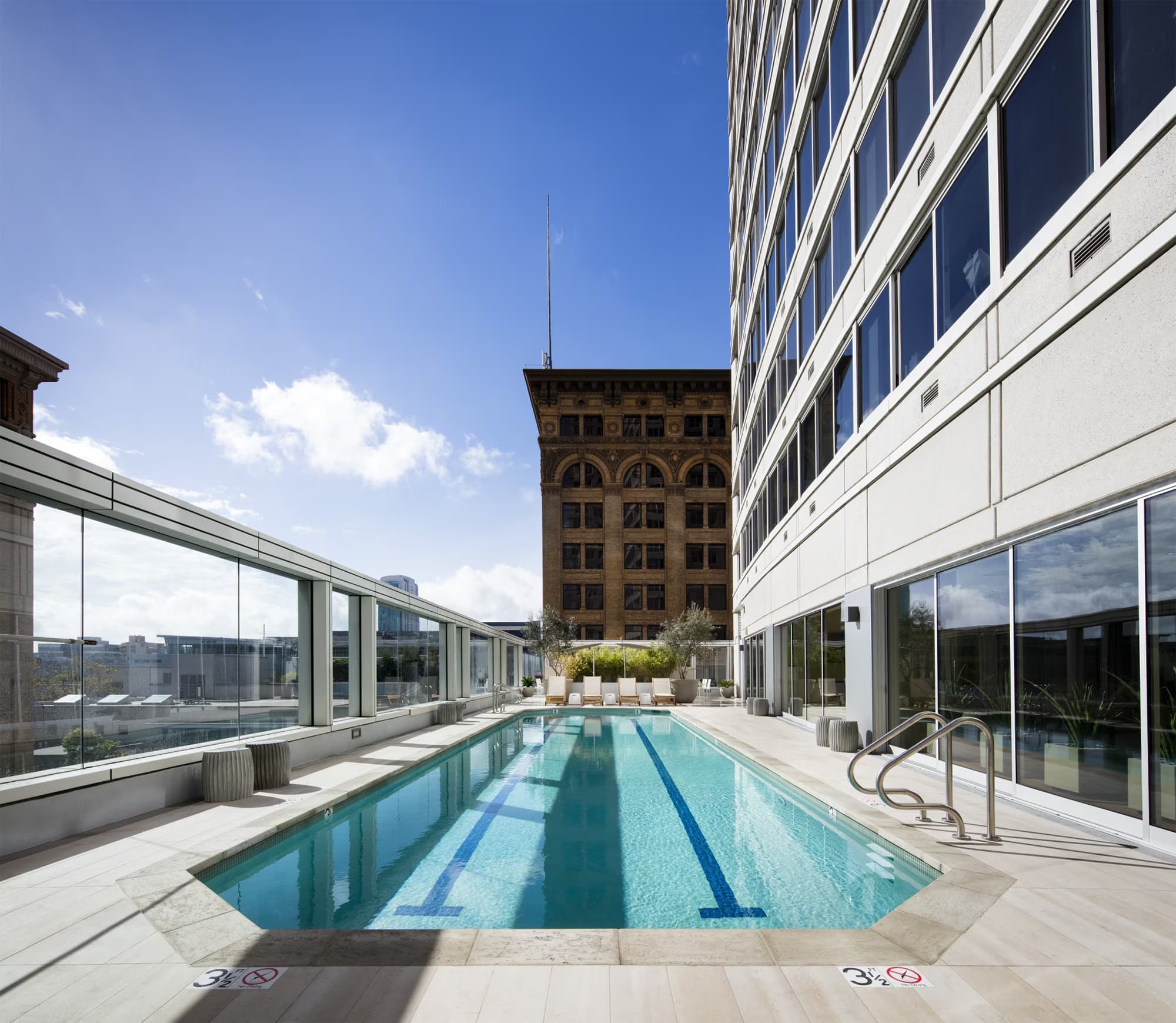 Rooftop lap pool with lane markings, glass railings, lounge seating, and San Francisco cityscape views.