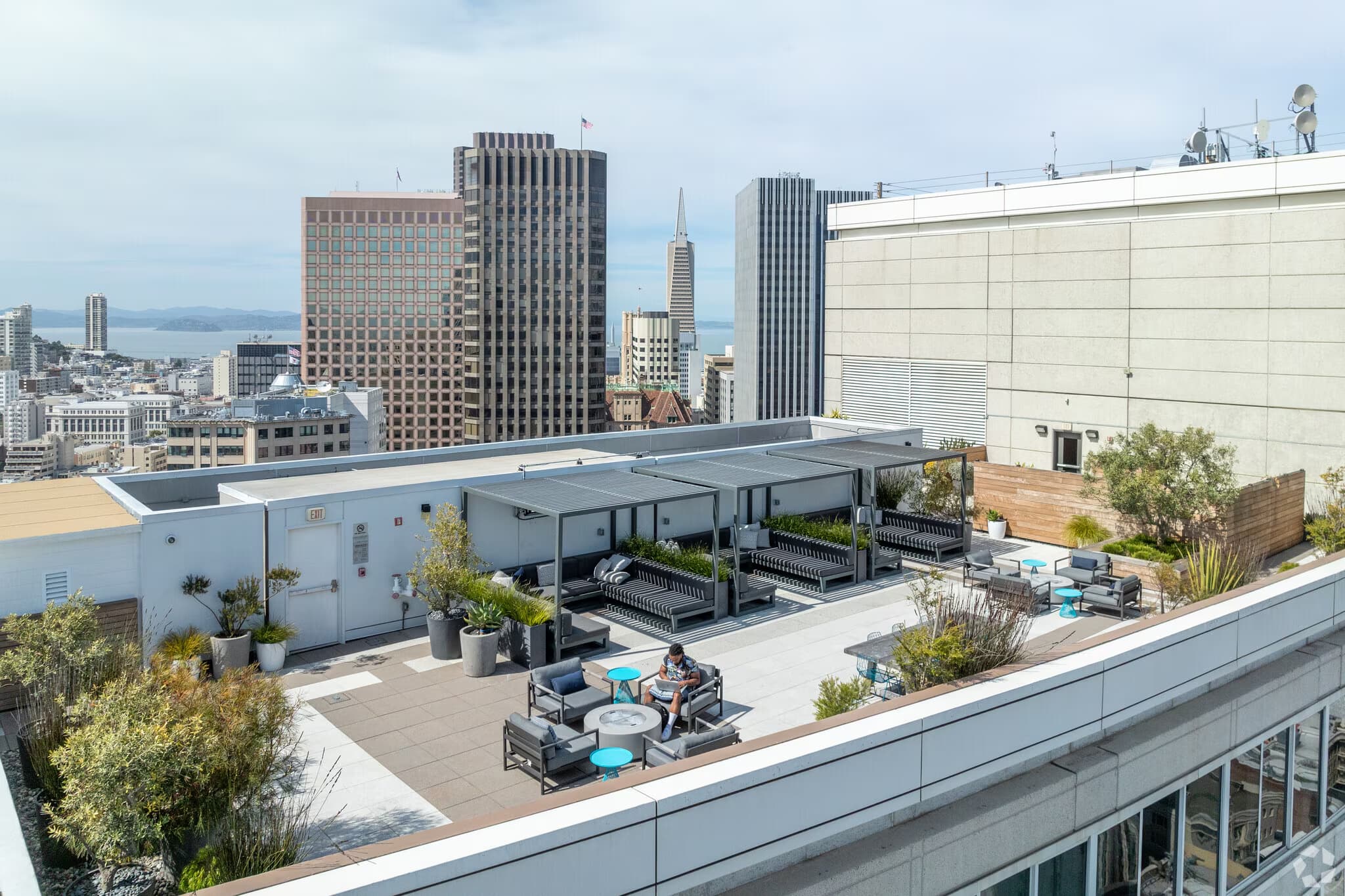 Rooftop terrace with seating areas, potted plants, and San Francisco skyline including Transamerica Pyramid in background.