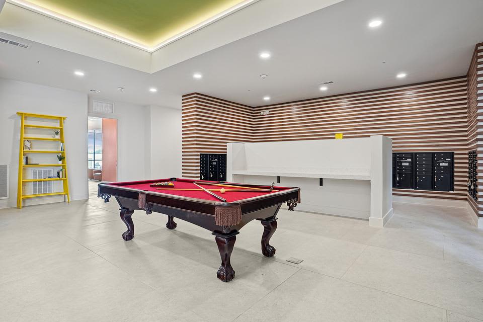 Game room with red felt pool table, wood and white striped accent wall, yellow shelving unit, and recessed ceiling lights.