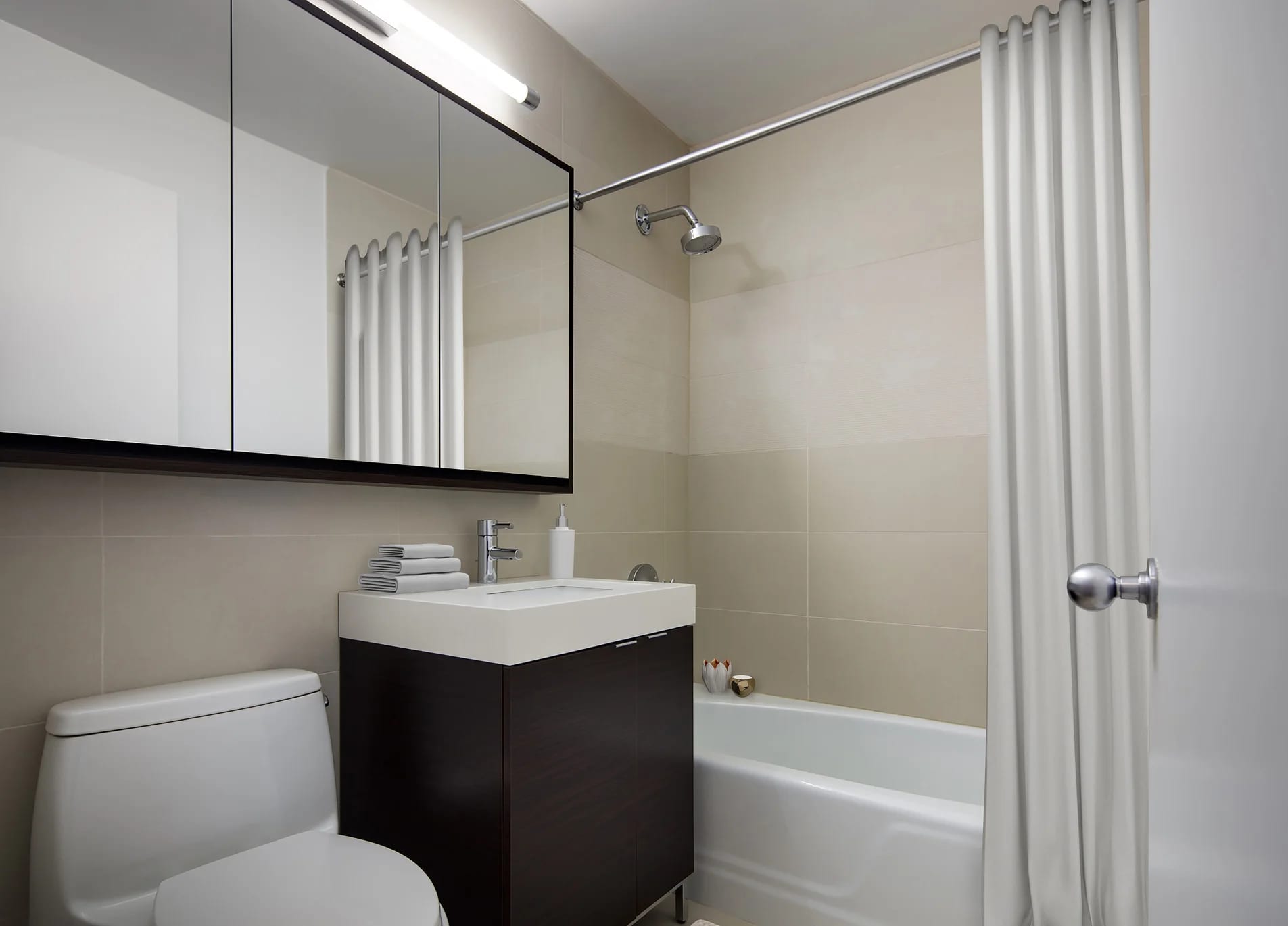 Modern bathroom with black vanity, white sink, mirrored medicine cabinet, white subway tile walls, and bathtub with shower enclosure.