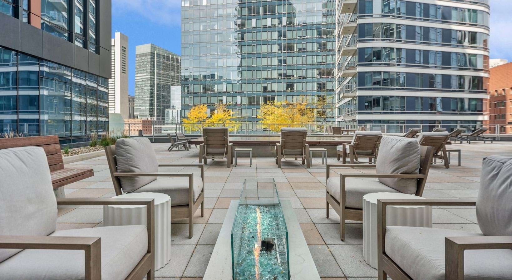 Rooftop terrace with wooden lounge chairs, cushioned seating, linear water feature, and downtown Boston skyline views.