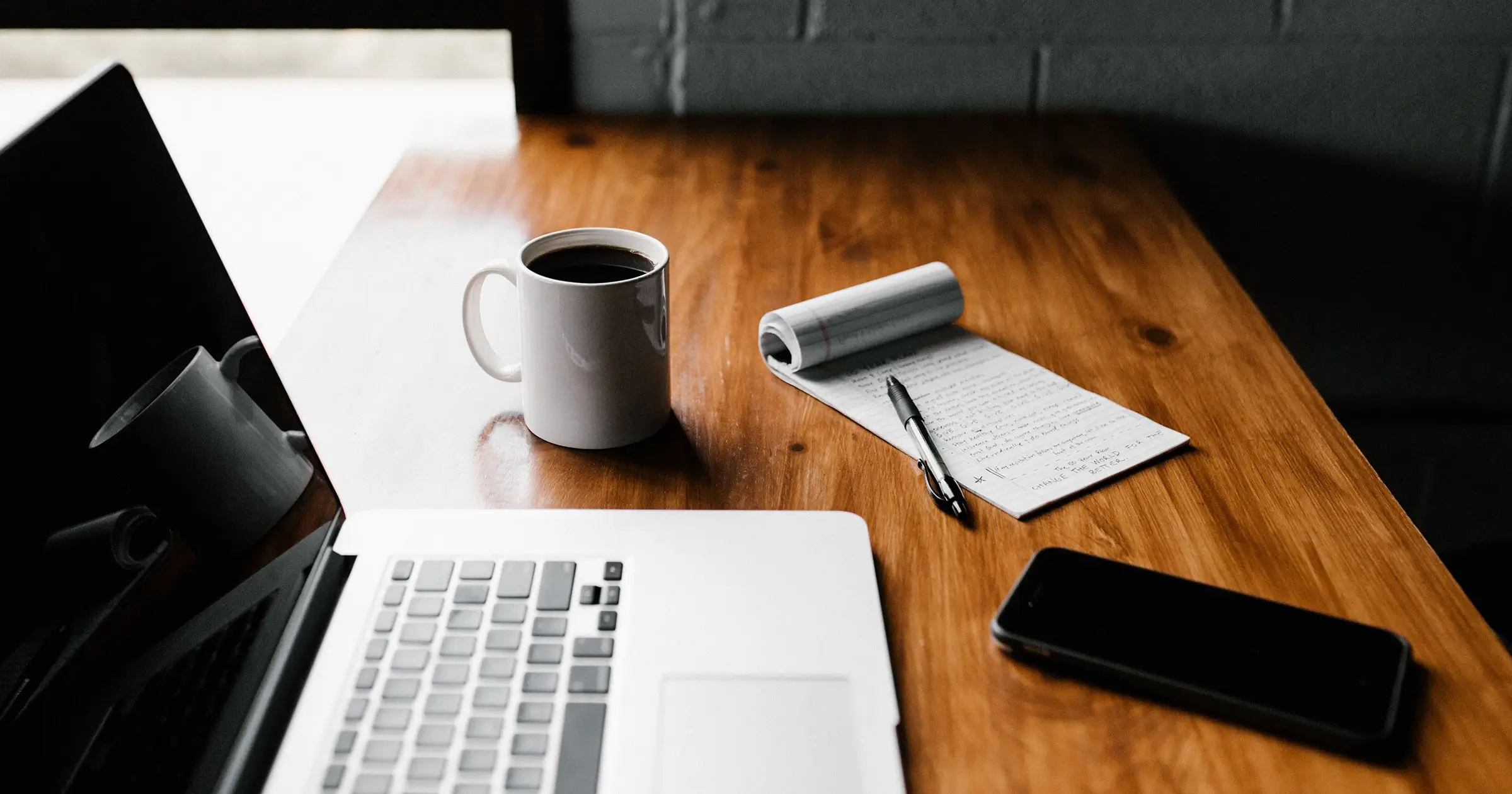 Wooden desk with laptop, notepad and coffee cup