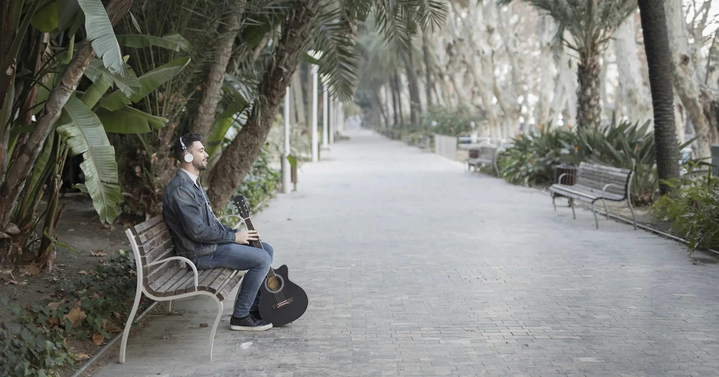 Man with a guitar sitting alone on a park bench