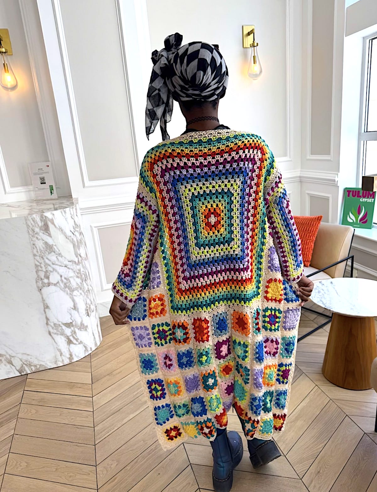 Rainbow patchwork crochet duster cardigan in a marble lobby