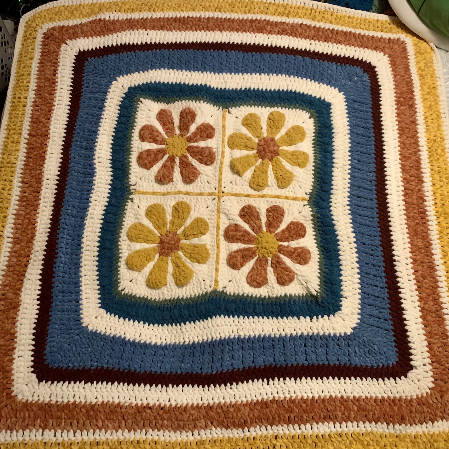 Crochet blanket with four large daisies in rust and gold
