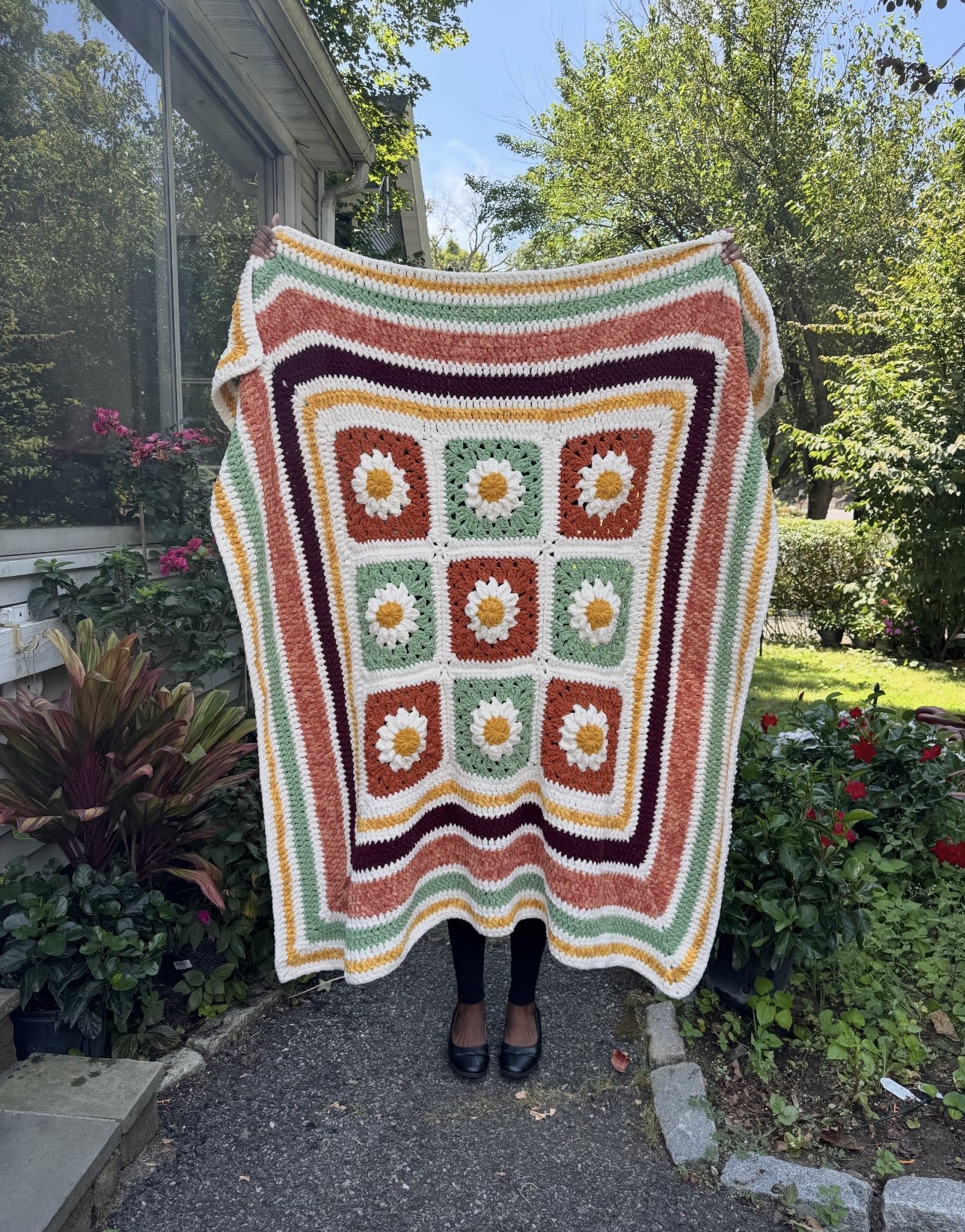 Selena holding up a handmade autumn daisy granny square blanket