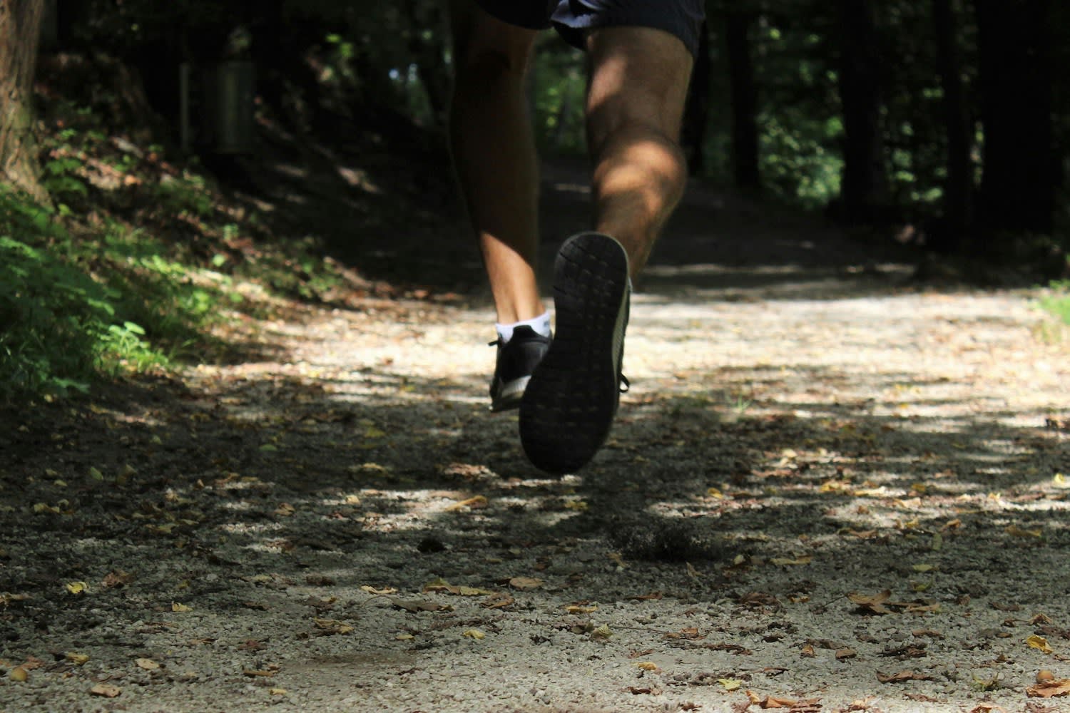 Runner’s legs on a forest trail, showing foot strike and cadence while running in black shoes