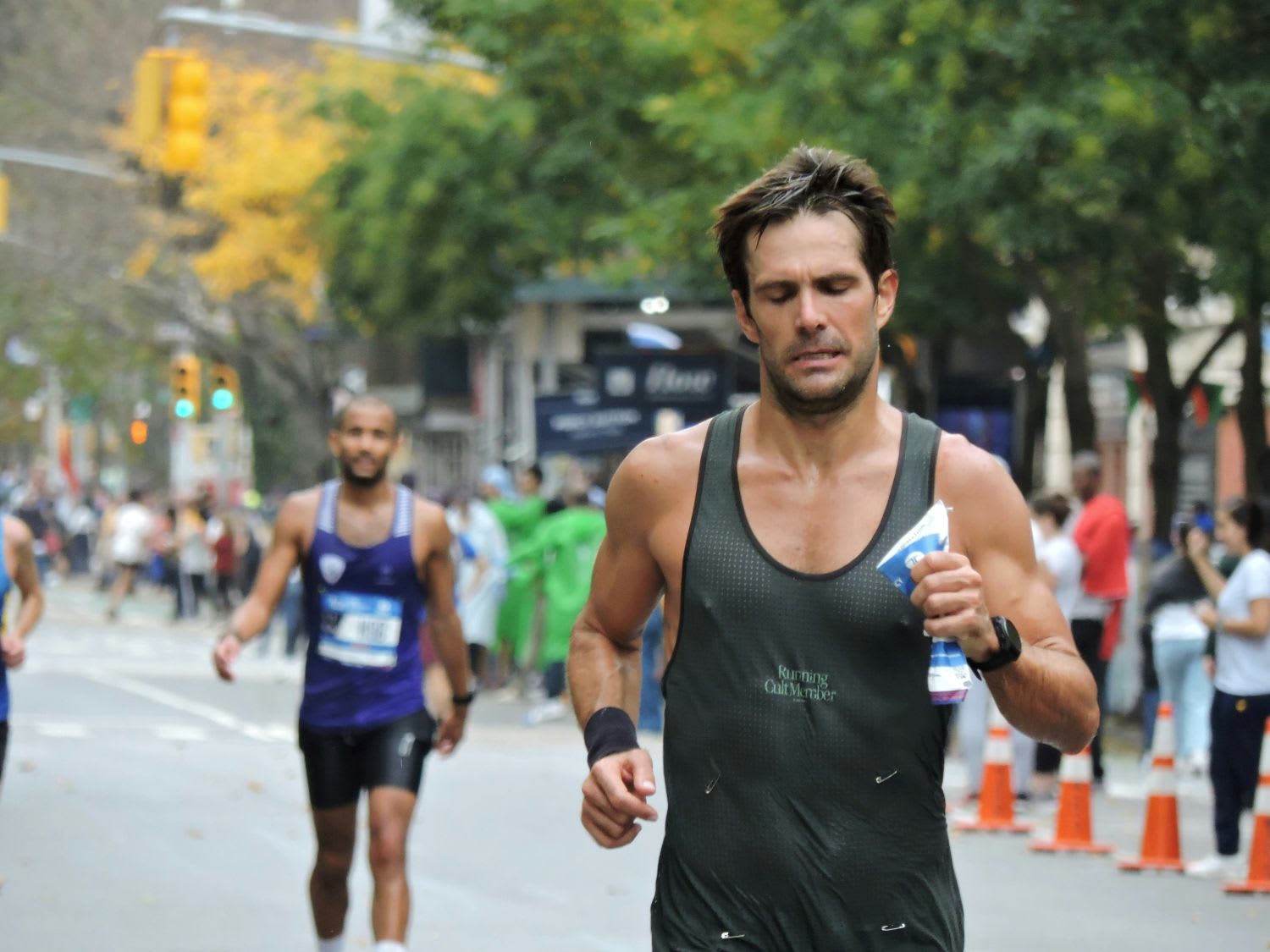 Corredor con camiseta de "Running Cult Member" y expresión de esfuerzo compitiendo en una carrera