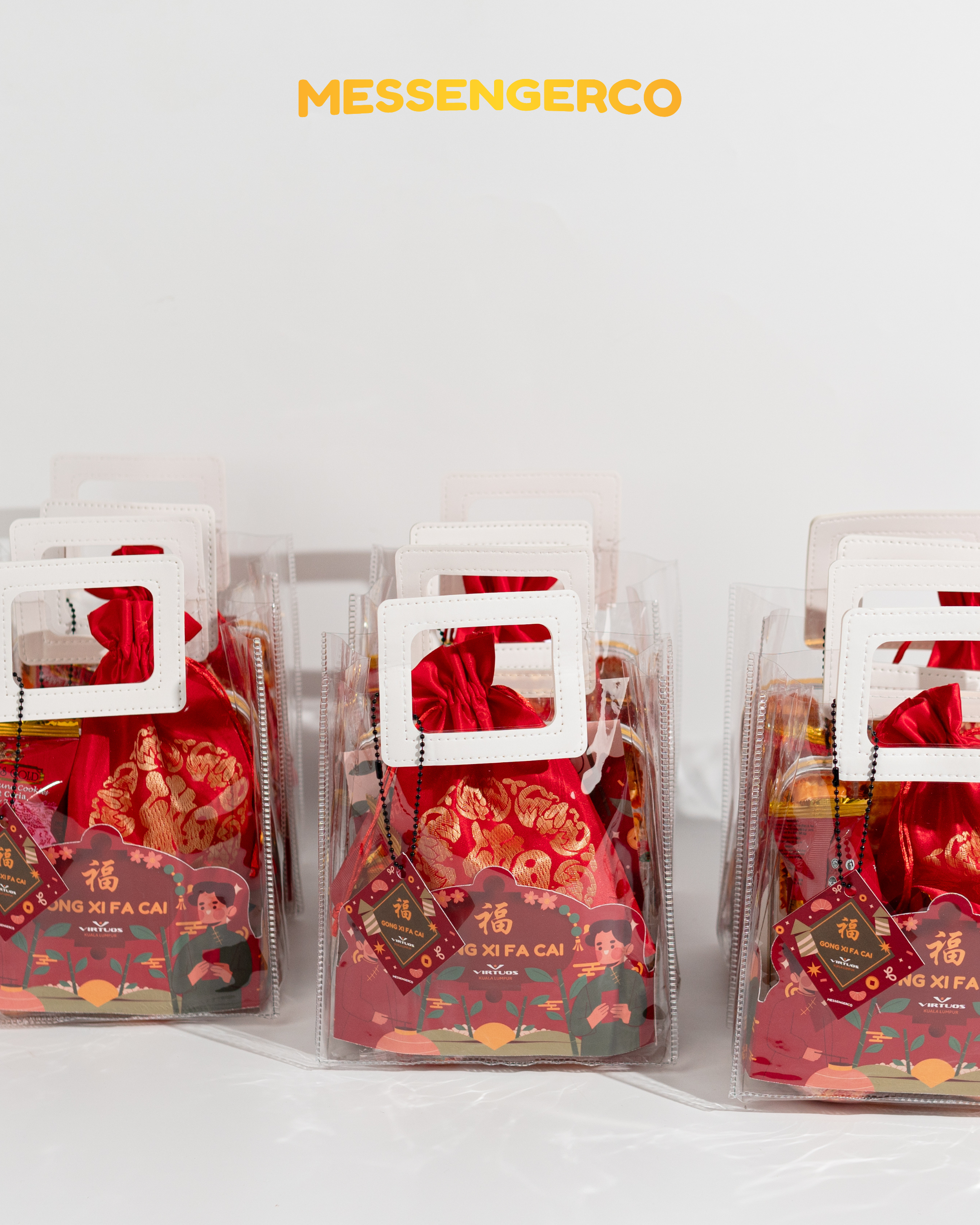 Rows of Messengerco Care Package CNY gifts for Virtuos in clear totes with white handles, red pouches and Gong Xi Fa Cai cards.