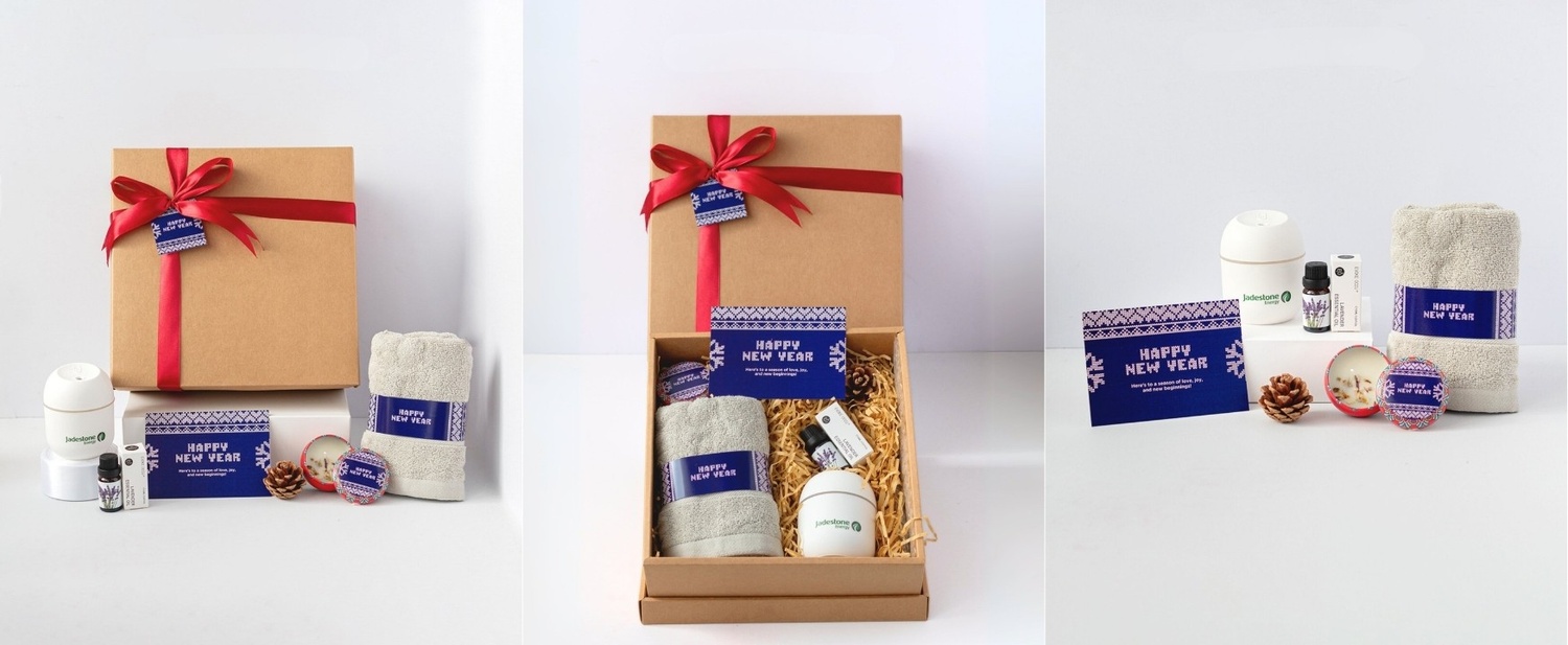 Wellness Christmas gift set featuring a kraft gift box with red ribbon, towel, essential oil diffuser, lavender essential oil, festive candle, pinecone and a Happy New Year greeting card, curated for Jadestone corporate gifting.