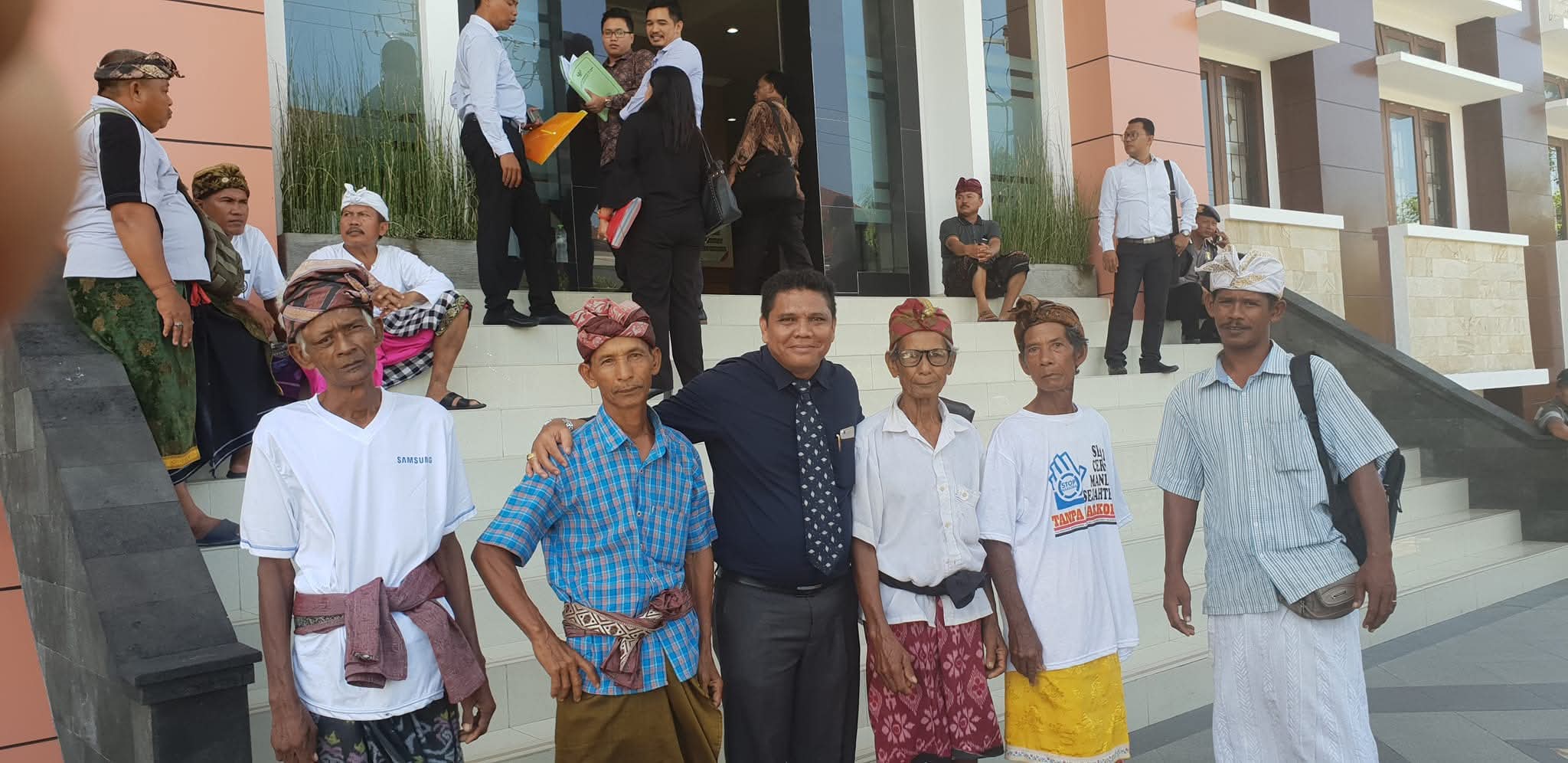 Momen Raymond Simamora, S.H., M.H. (tengah) yang mengenakan kemeja biru tua dan dasi, berpose bersama sekelompok warga di depan gedung Pengadilan Negeri Slawi.