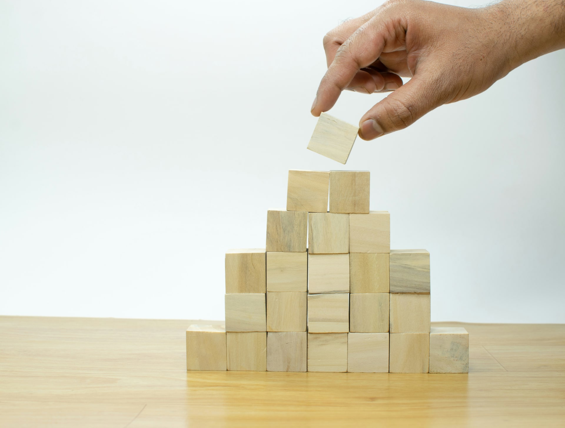 Hand placing the top wooden block on a stacked pyramid
