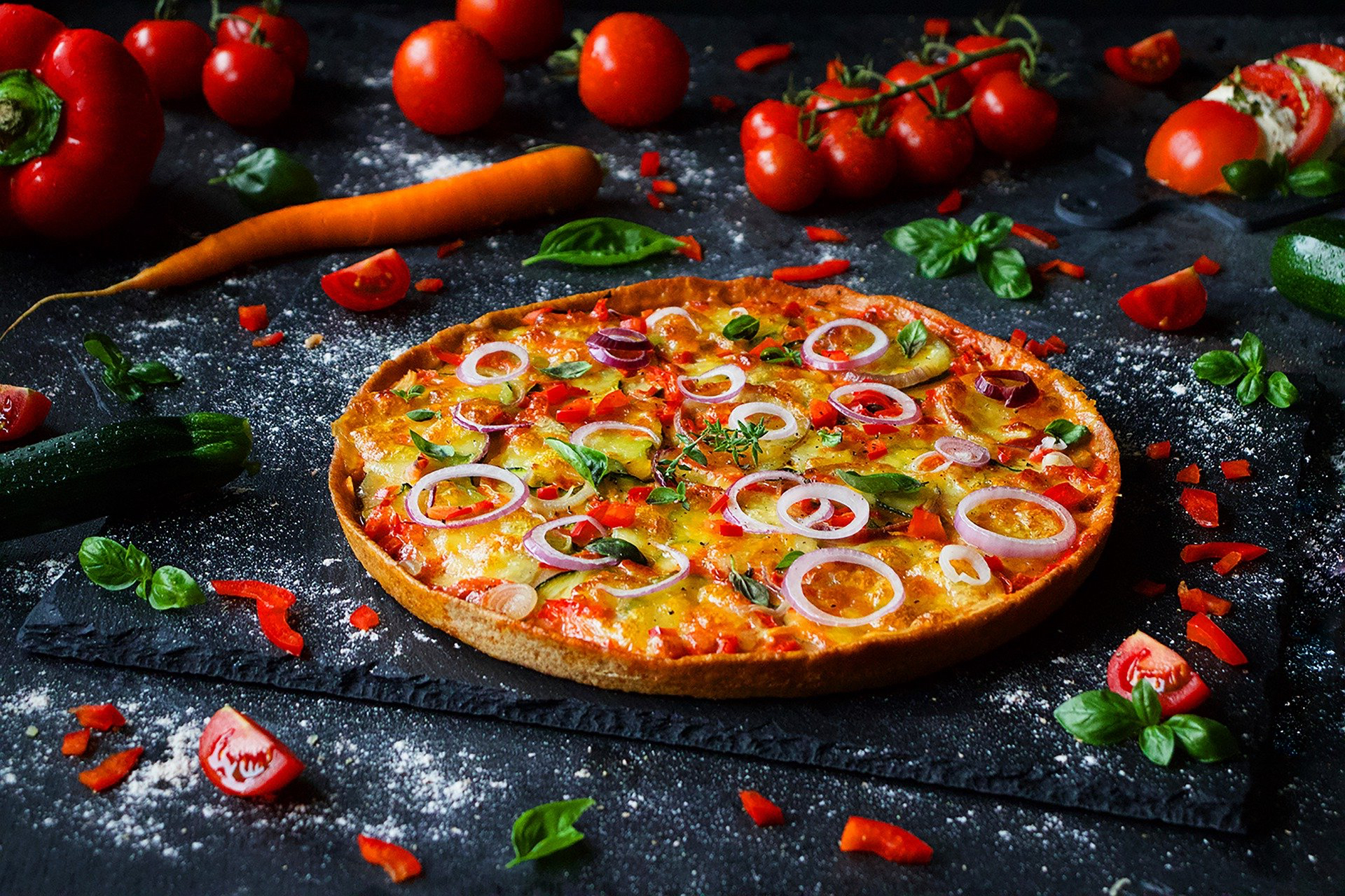 Pizza otoczona bazylią, pomidorami, marchewką, cukinią i papryką