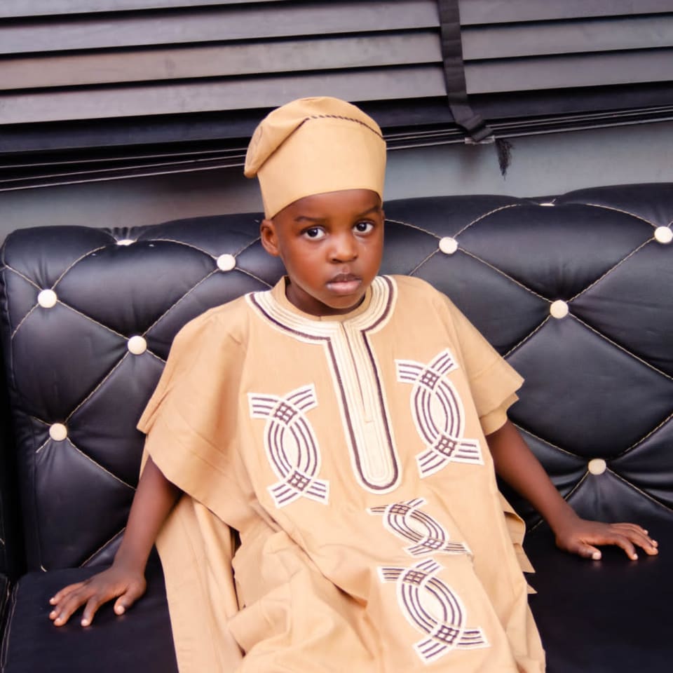 Young boy in a gold agbada and fila seated on a sofa